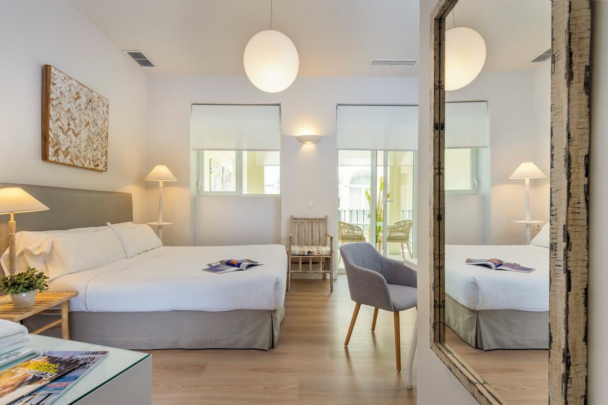A hotel room with two beds, a chair, a table with a lamp, and a large mirror.