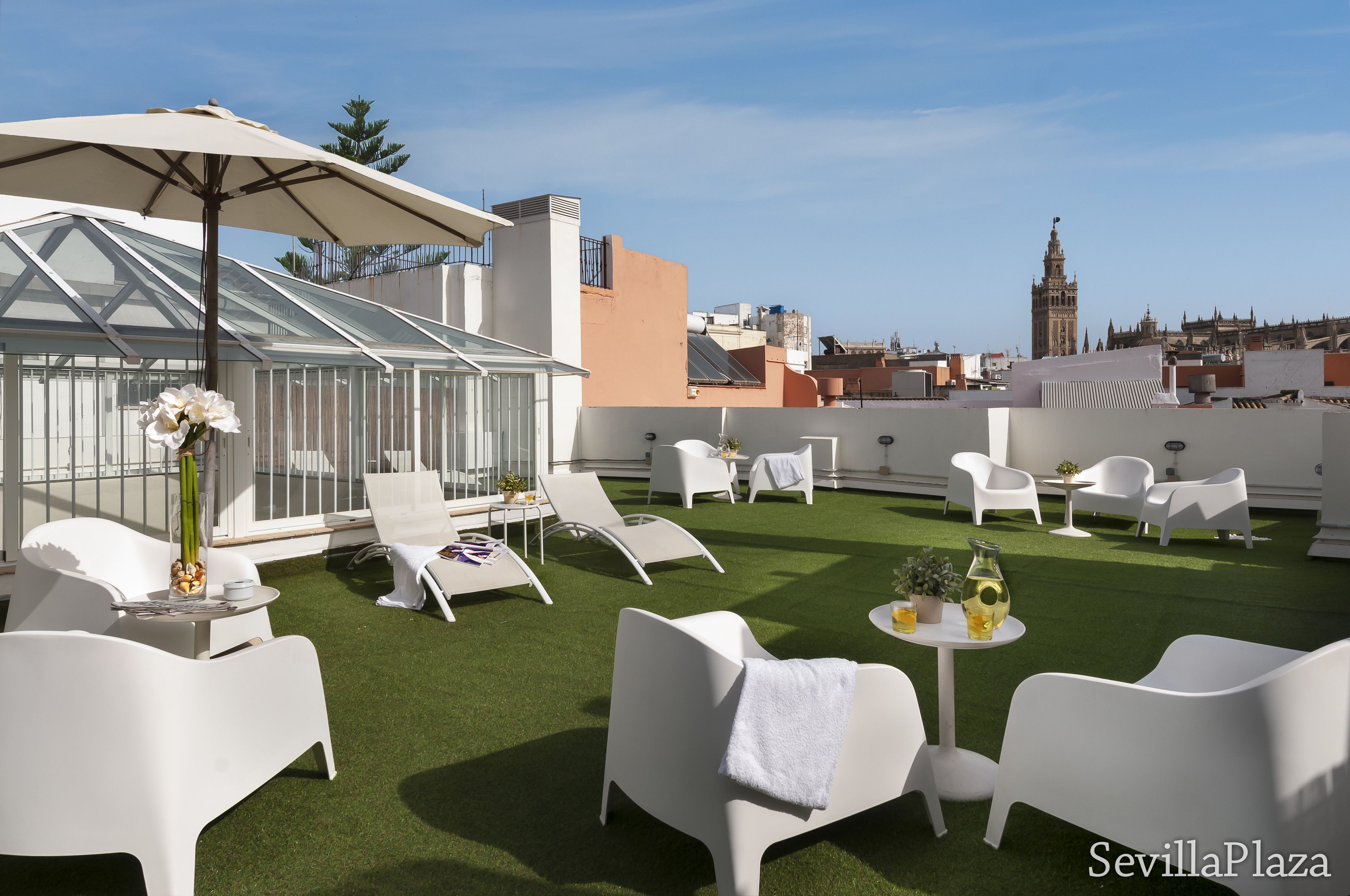 Une terrasse sur le toit, dotée de mobilier blanc, une serre et une vue sur le panorama urbain, notamment une tour.