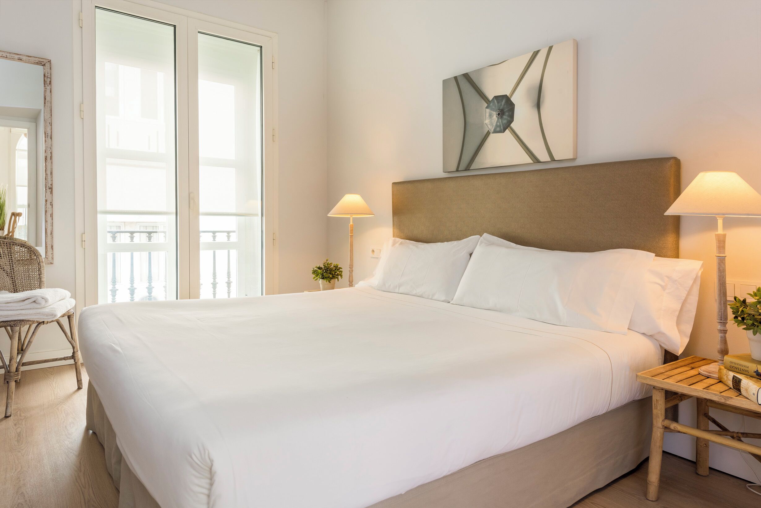 Une chambre d’hôtel avec un grand lit, deux lampes de chevet, une œuvre d’art accrochée au mur et une vue à travers une porte vitrée.