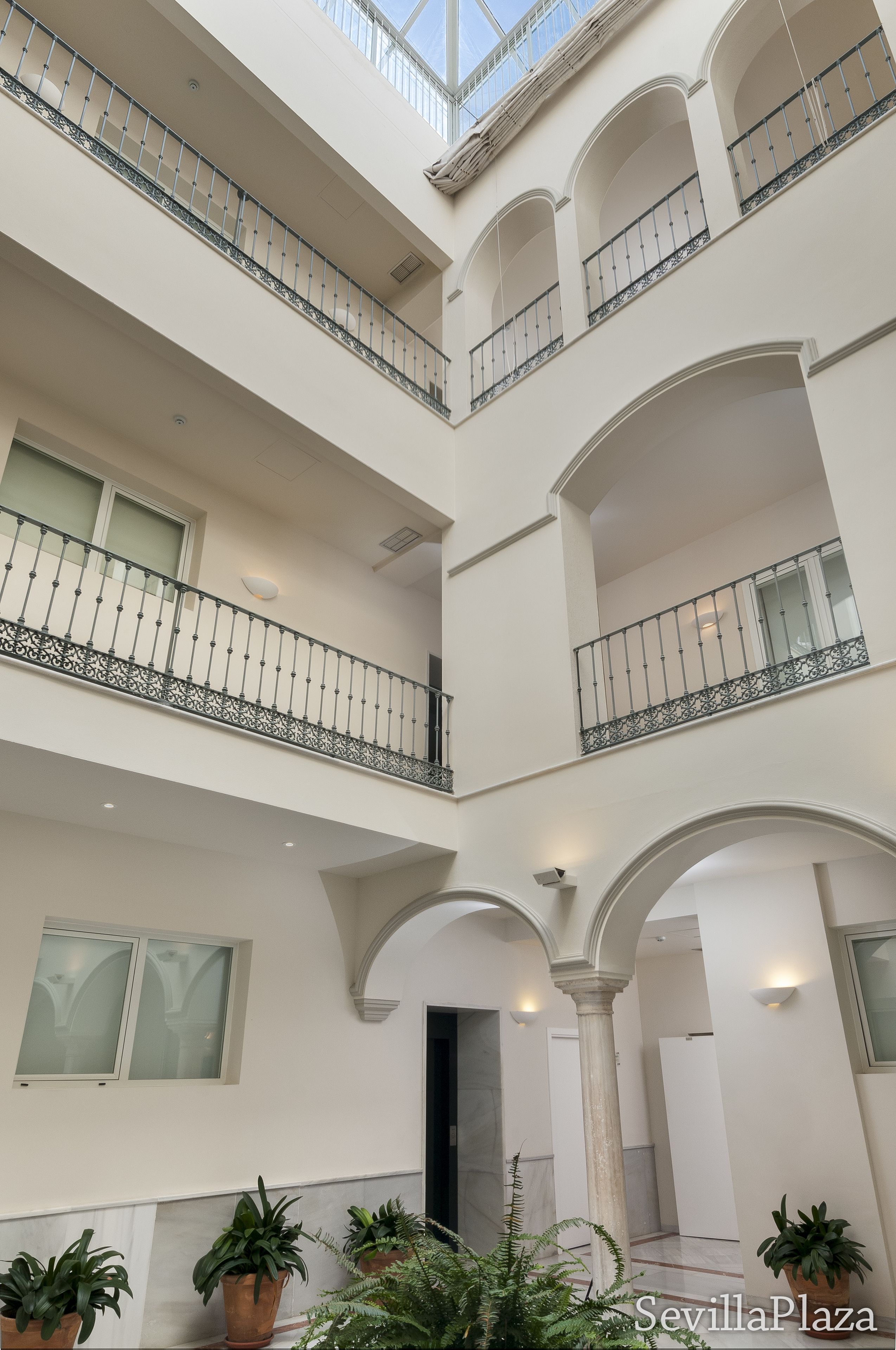 Un atrium à plusieurs niveaux, doté de balcons, de grandes fenêtres et de plantes en pot.