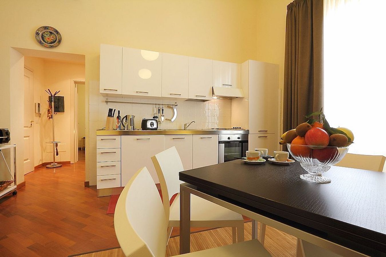Una cocina moderna con armarios blancos, encimera negra y un frutero sobre la mesa.