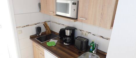 Cocina compacta con microondas, cafetera, tostadora y pileta.
