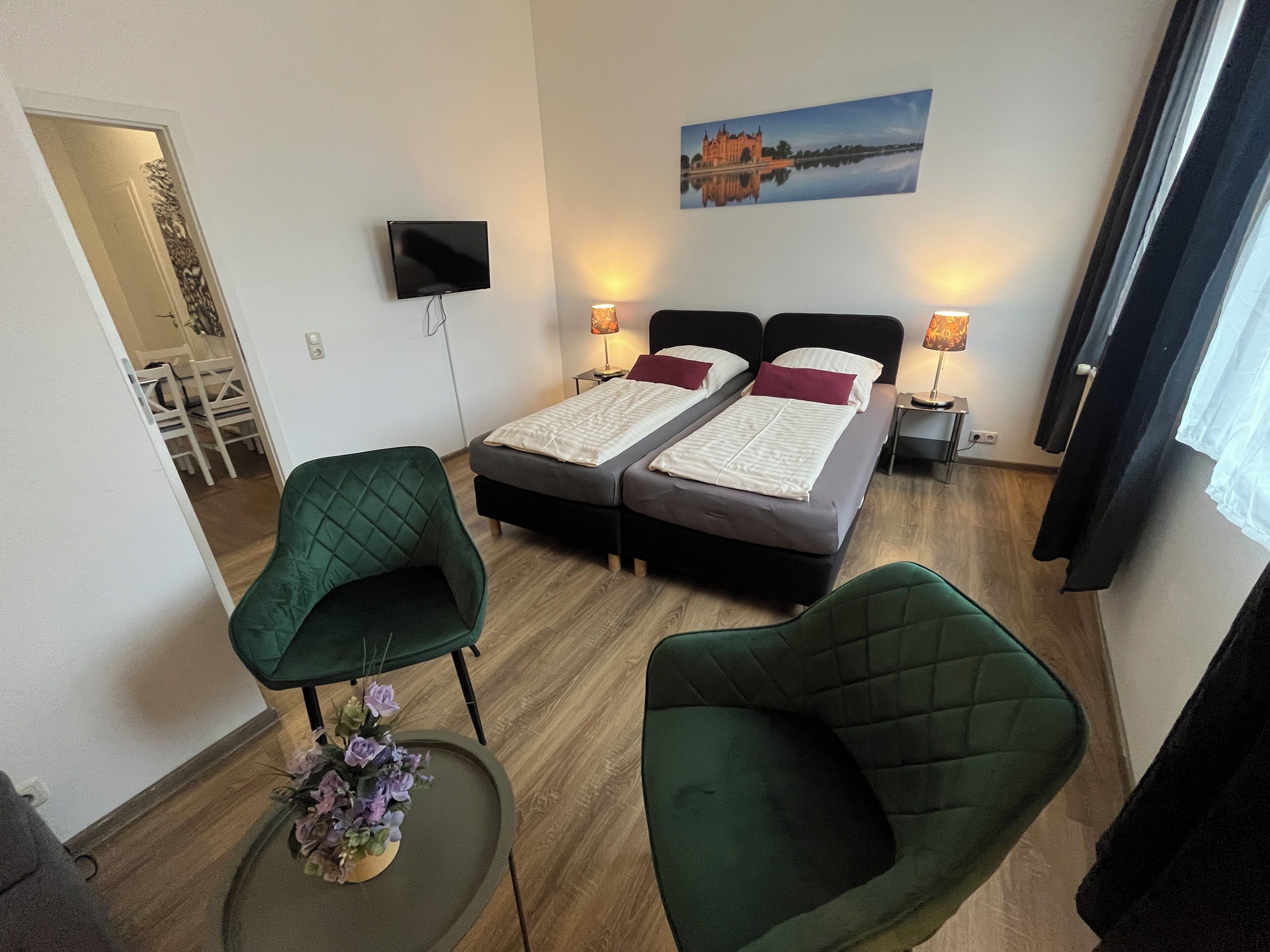 Ein Hotelzimmer mit zwei Betten, einem Fernseher, einem Gemälde und grünen Stühlen.