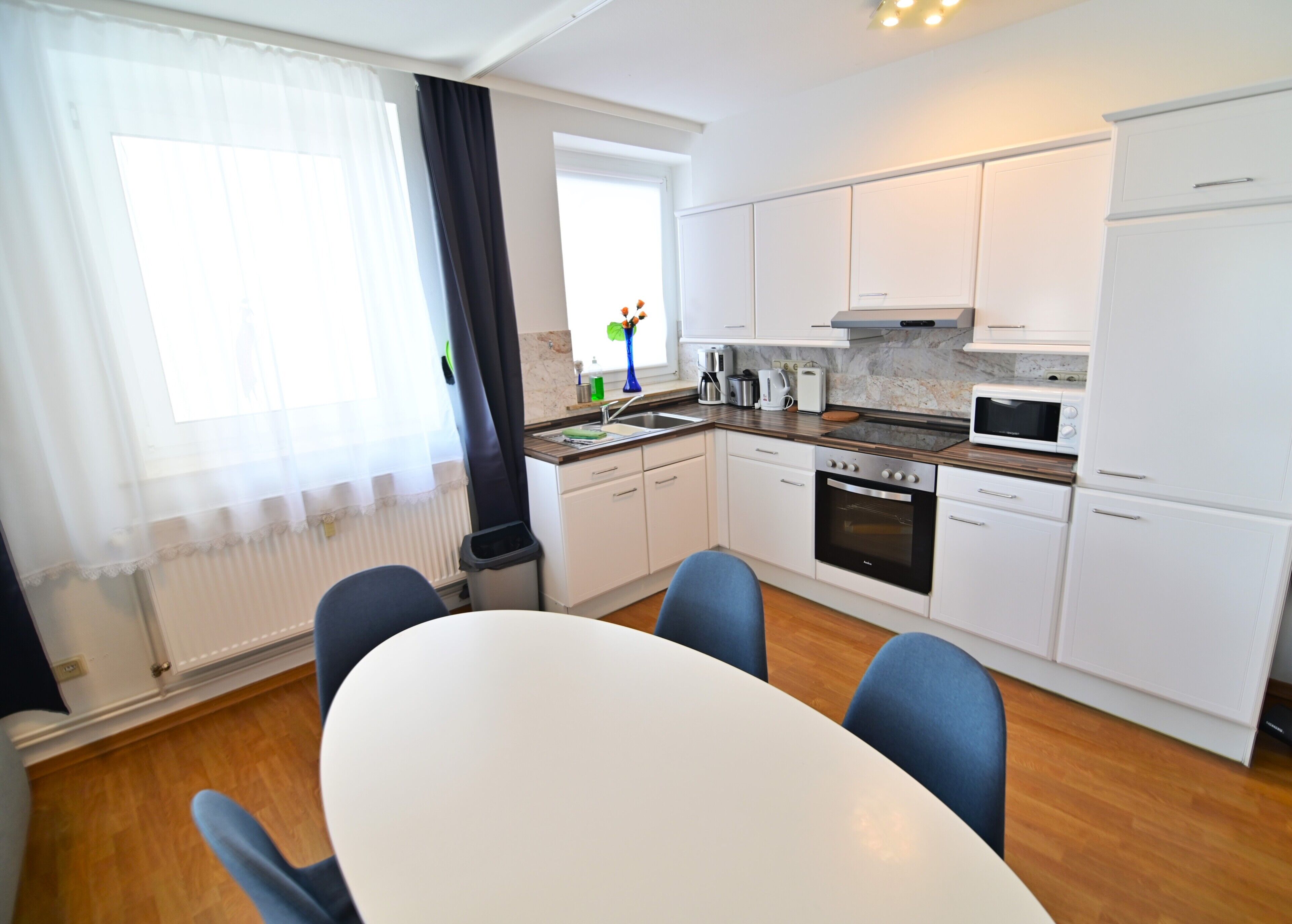 Une cuisine moderne avec des meubles blancs, une cuisinière, un four à micro-ondes et un coin repas comprenant une table et des chaises.