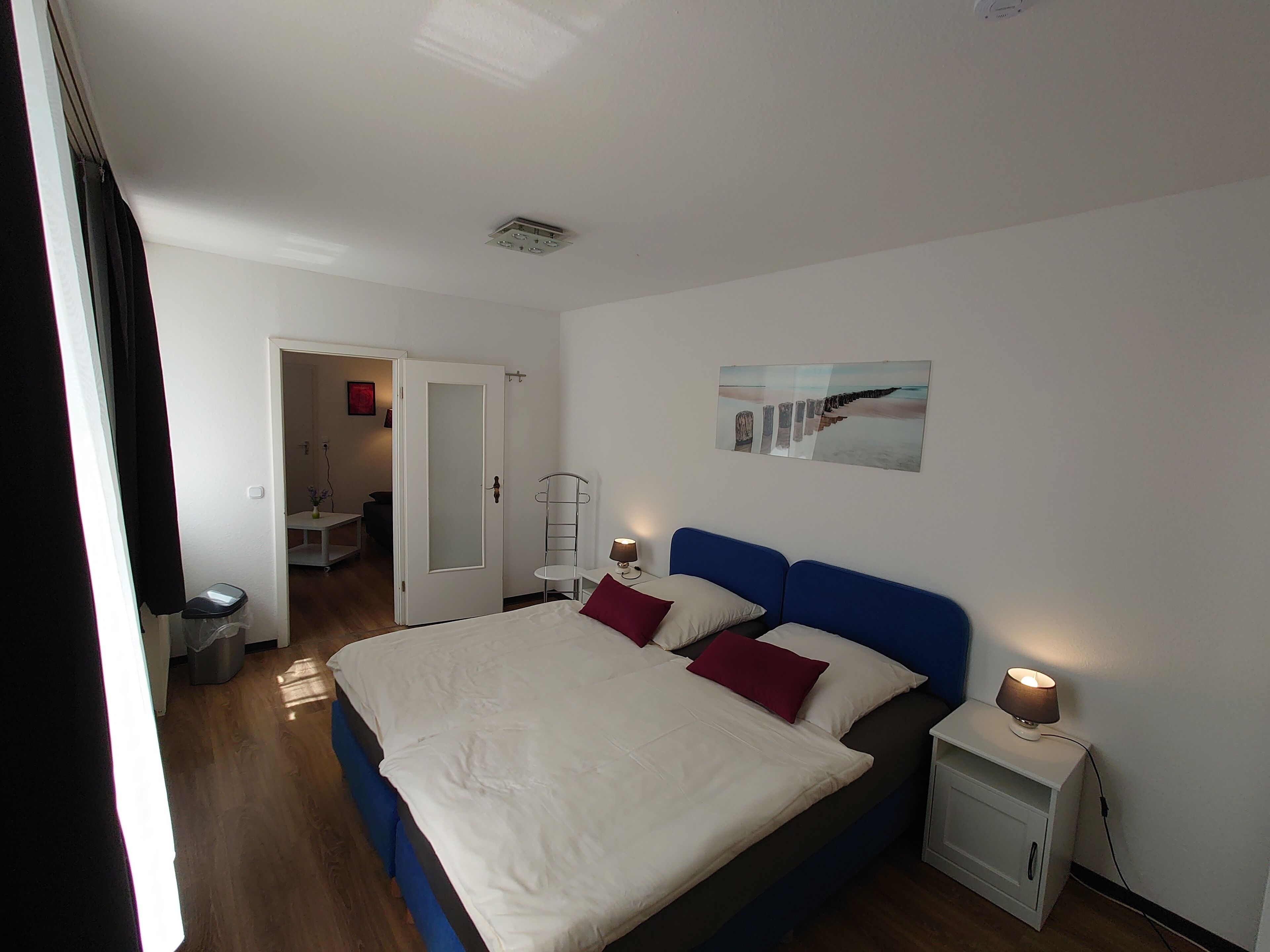 A bedroom with a bed, bedside table, lamp, and a painting on the wall.