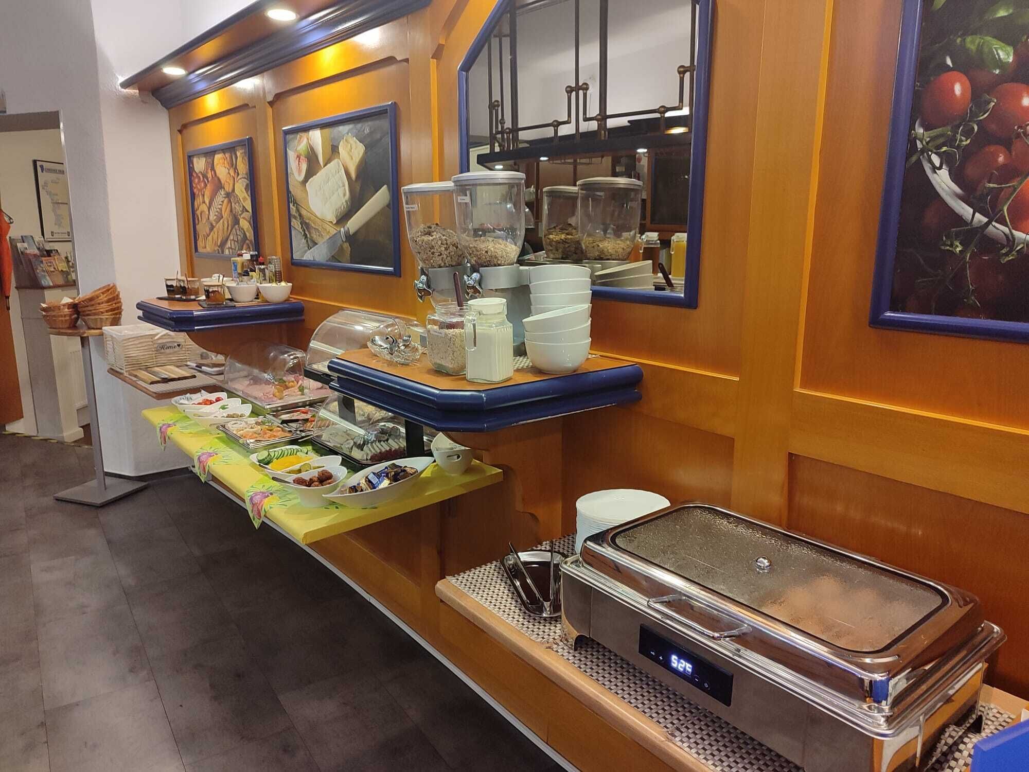 A buffet setup with various food items and containers, a digital clock, and a mirror on the wall.