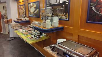 A buffet setup with various food items and containers, a digital clock, and a mirror on the wall.