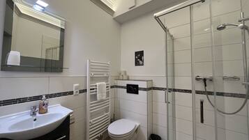 Un baño moderno con lavamanos, inodoro y ducha con mampara de vidrio.