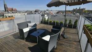 Una terraza en la azotea con mobiliario de mimbre, una mesa y una sombrilla.