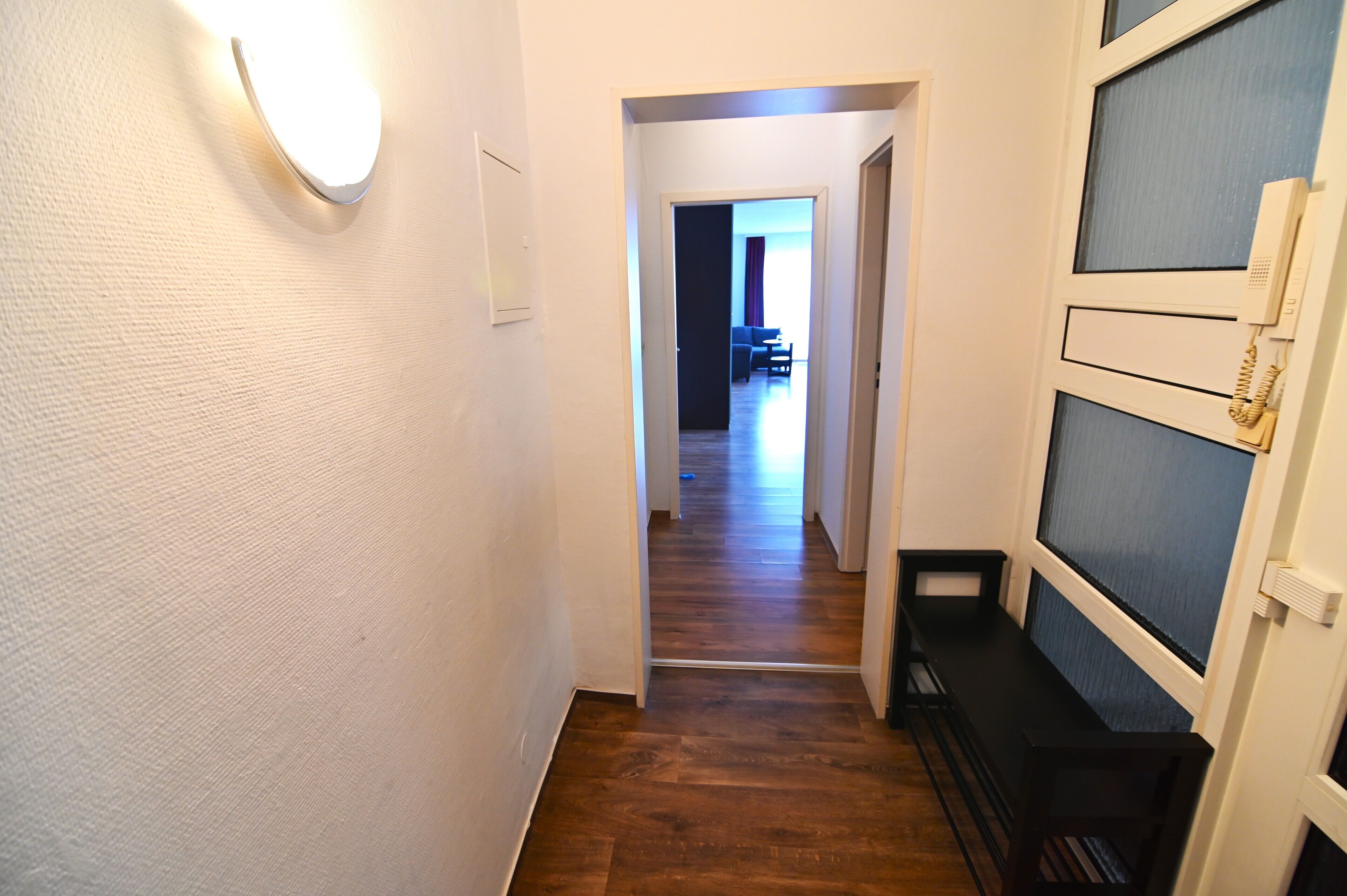 A hallway with a wooden floor, a light fixture, and a telephone on the wall.
