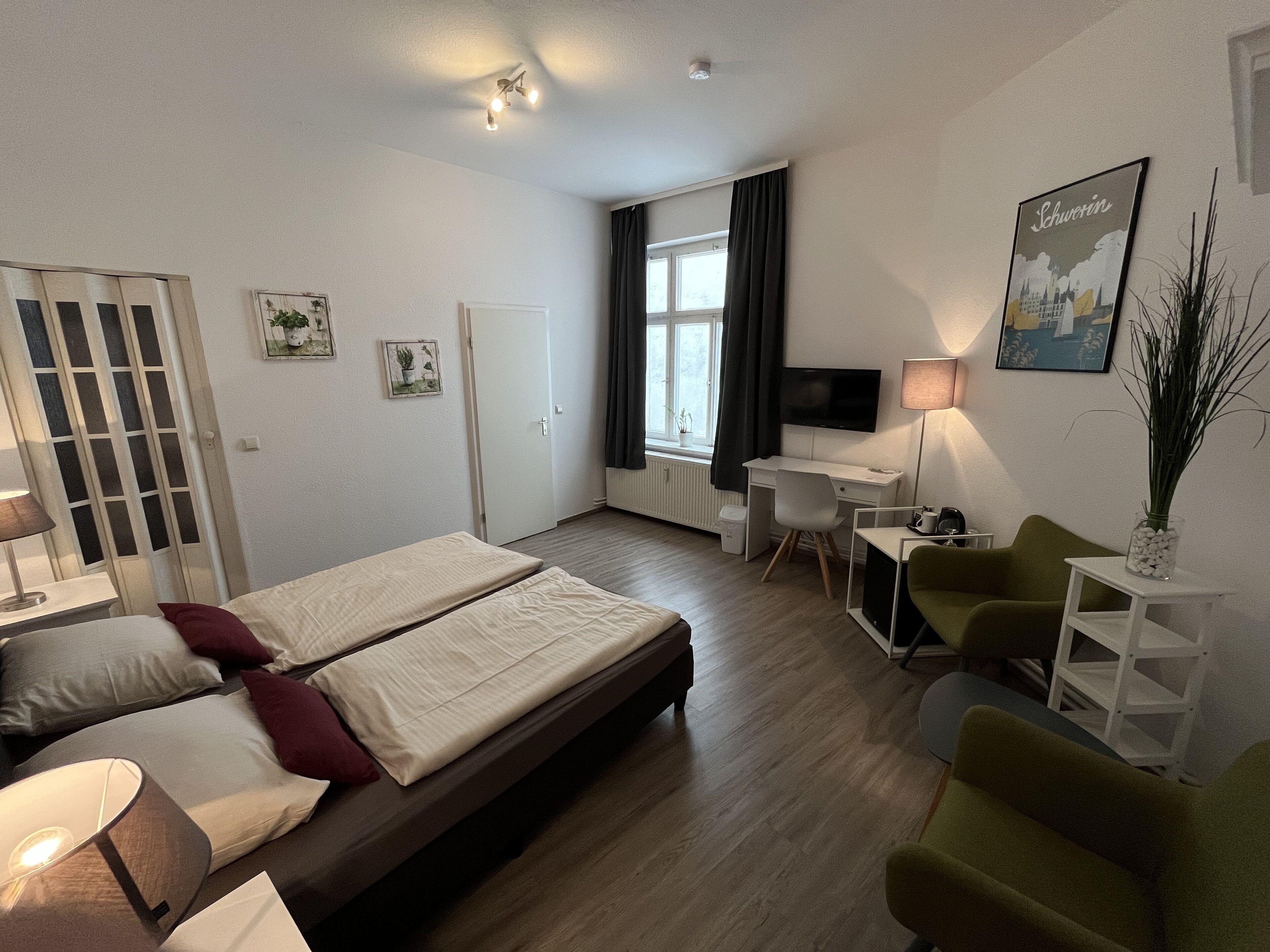 A hotel room with a bed, a desk, a chair, a TV, and a window with curtains.