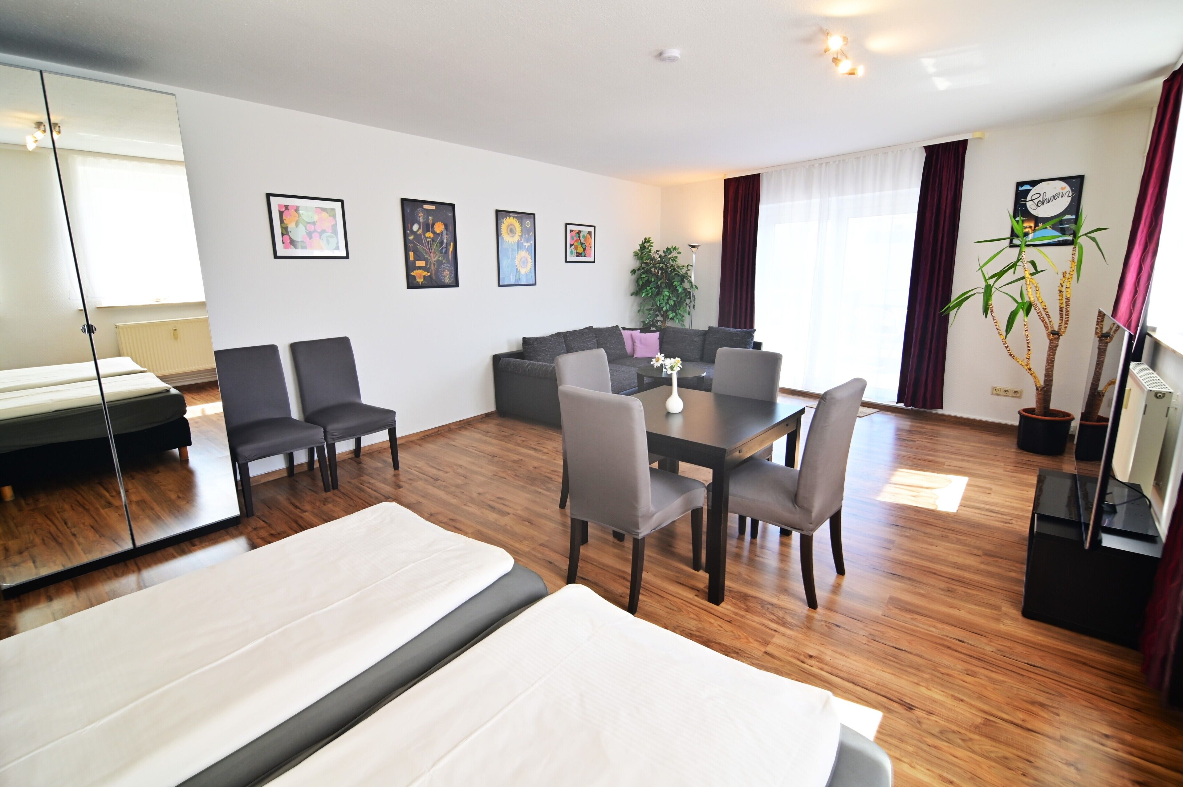 A modern hotel room with a bed, a sofa, a dining table with chairs, and a large mirror.