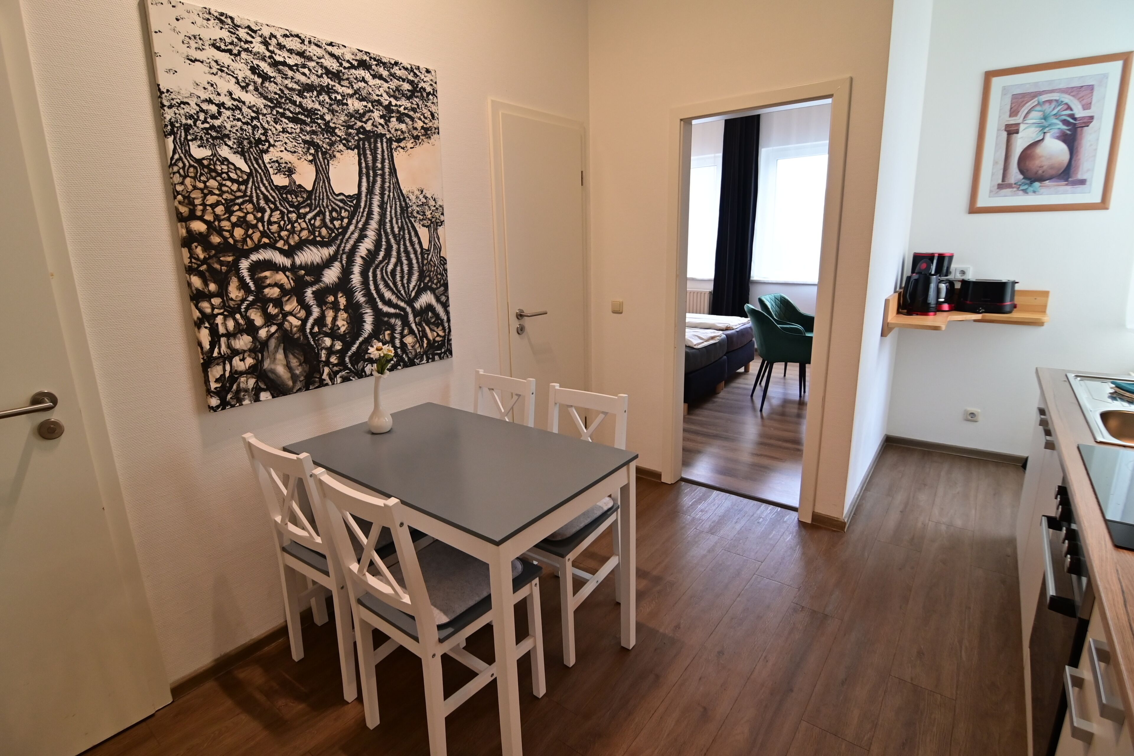 Uma área de refeições com mesa e cadeiras, um quadro na parede e uma cozinha com pia e fogão.