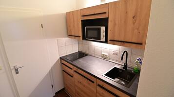 A compact kitchen with wooden cabinets, a built-in microwave, a sink, and a stainless steel faucet.