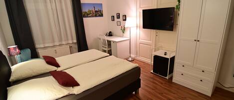 Un dormitorio con una cama doble, un escritorio, una silla, un televisor, un armario y un radiador.