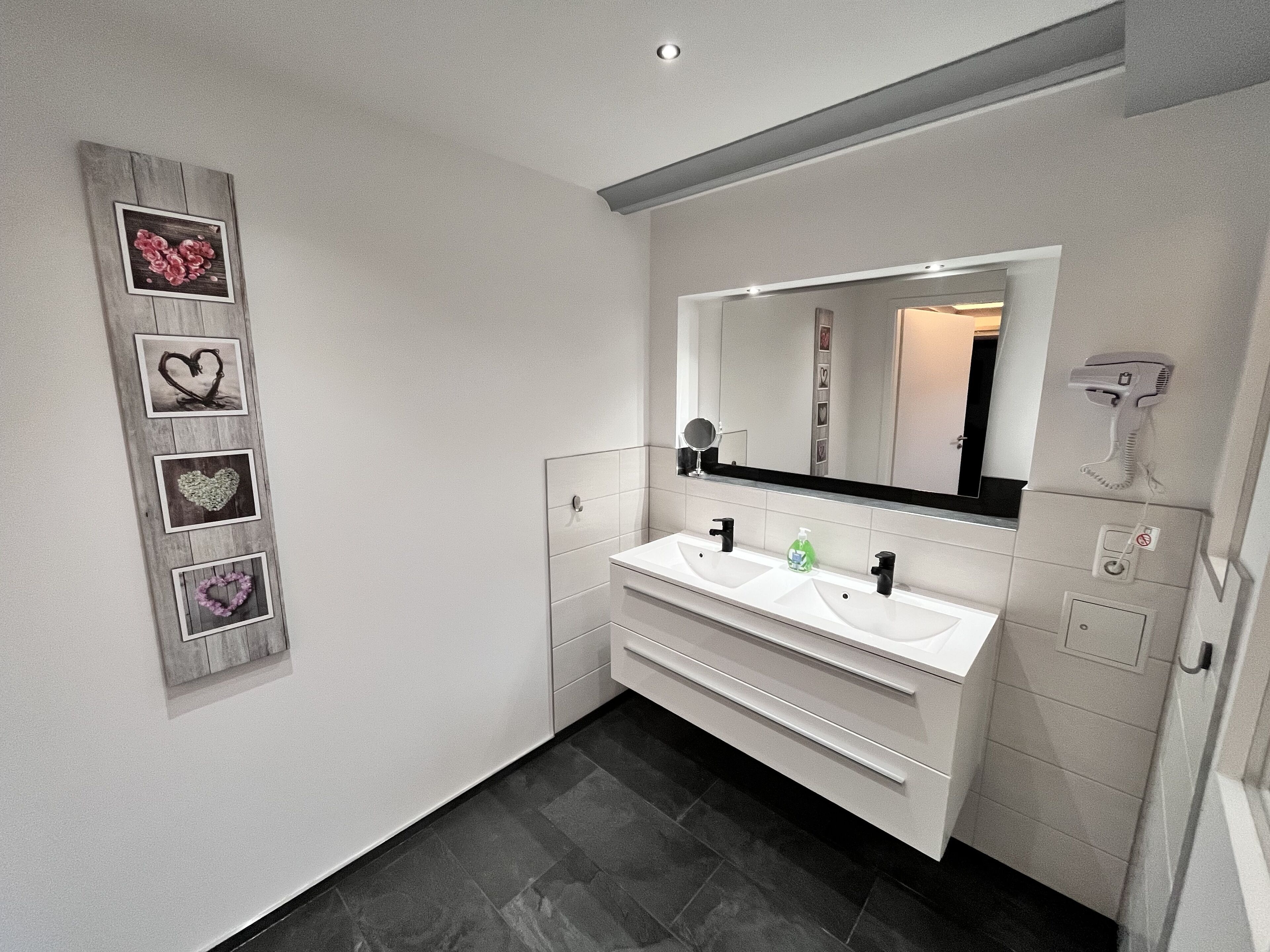 A modern bathroom with a white vanity, a large mirror, and a wall-mounted hairdryer.