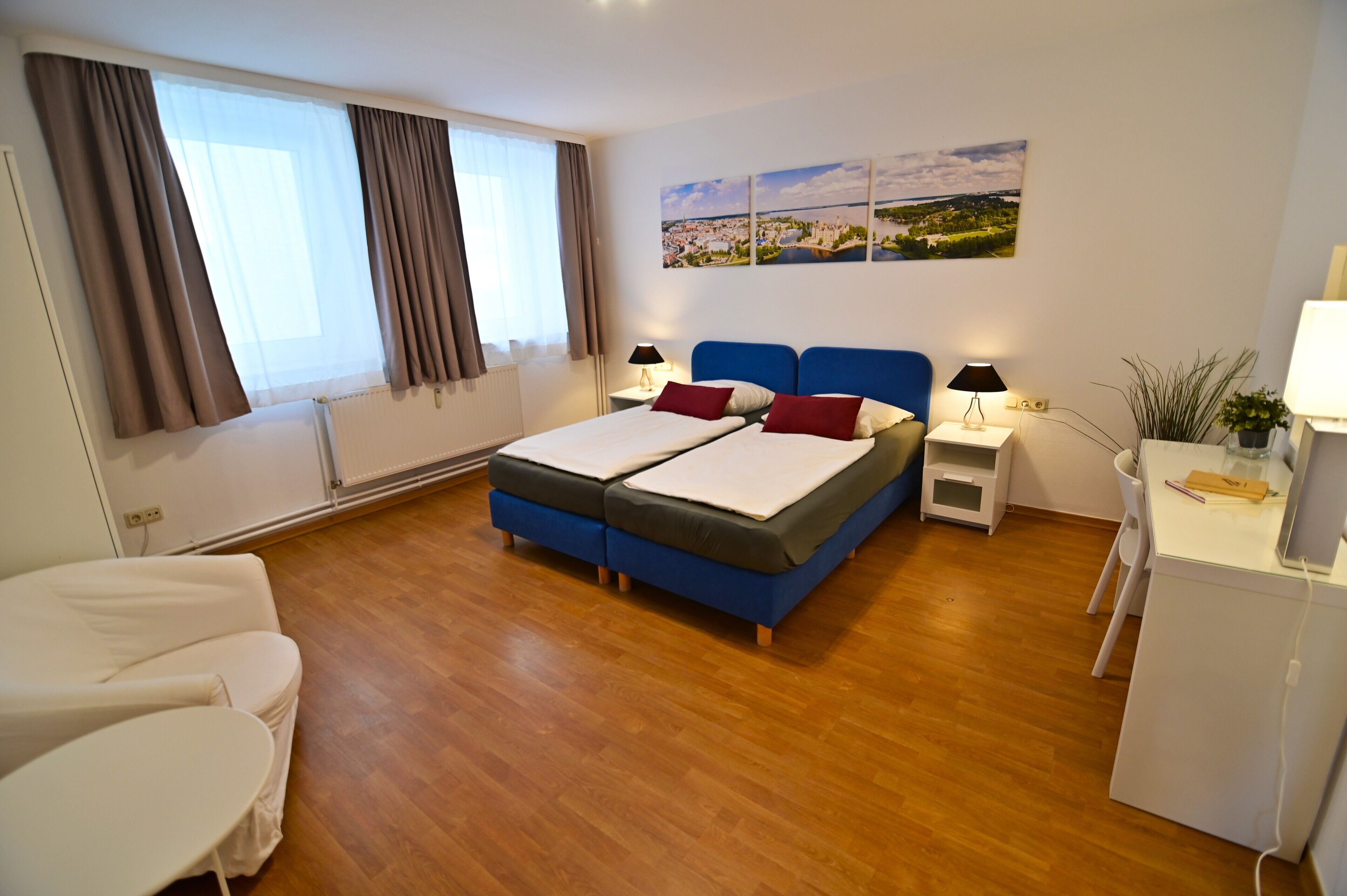 Un dormitorio con una cama doble, un escritorio con silla, una mesita y una ventana con cortinas.