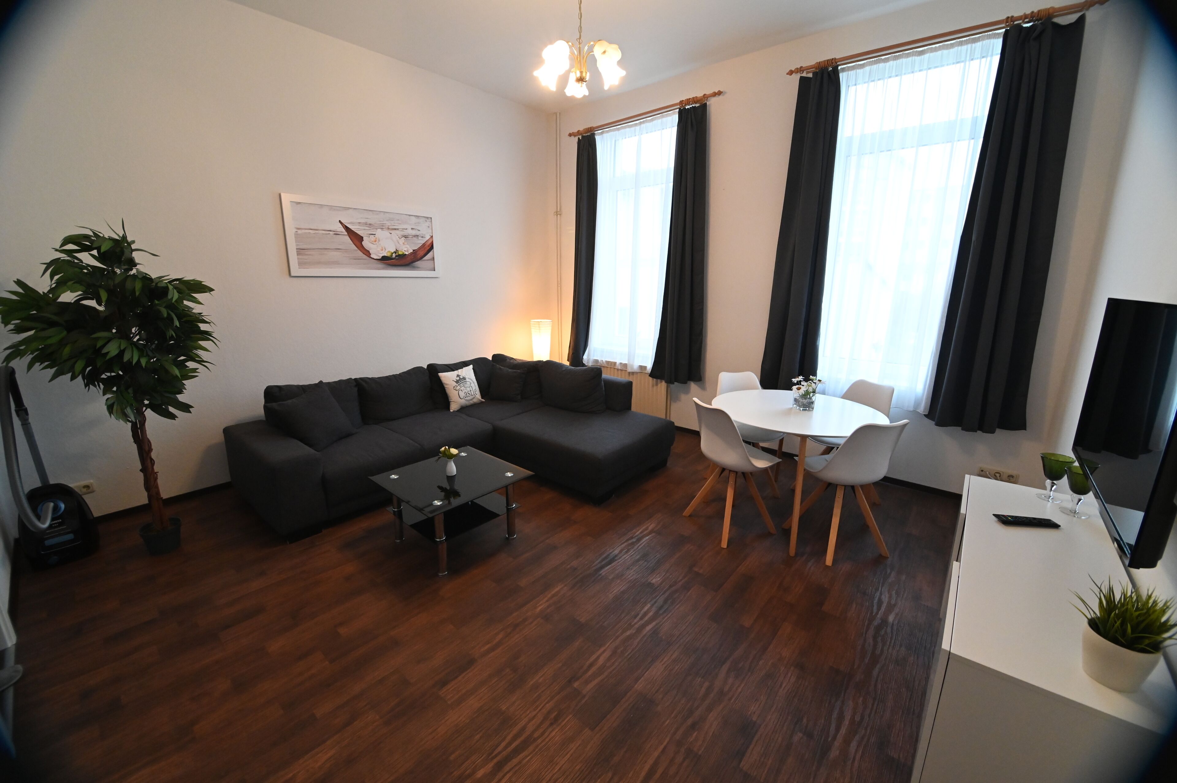 A modern living room with a sectional sofa, a dining table with chairs, a small coffee table, and a potted plant.