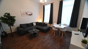 A modern living room with a sectional sofa, a dining table with chairs, a small coffee table, and a potted plant.