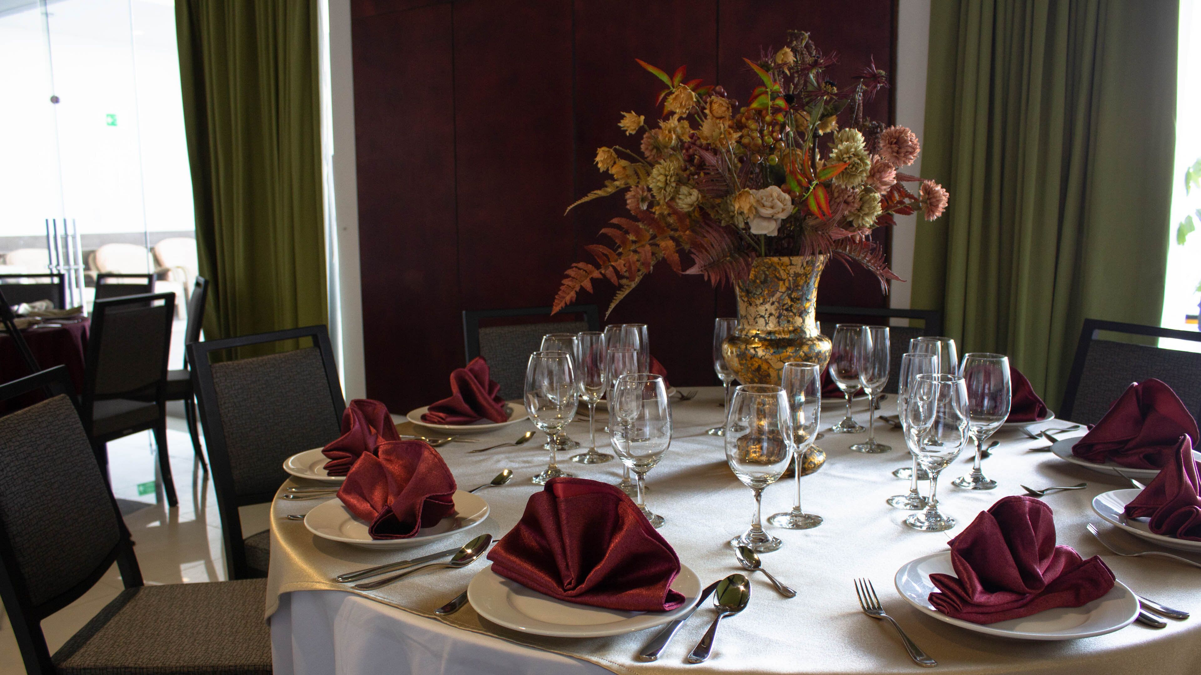 A dining table set for a meal with a vase of flowers in the center, surrounded by empty wine glasses and folded napkins.