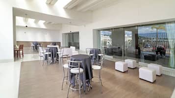 Un área de comedor moderna con mesas y sillas redondas, un separador de vidrio y vistas al paisaje urbano.