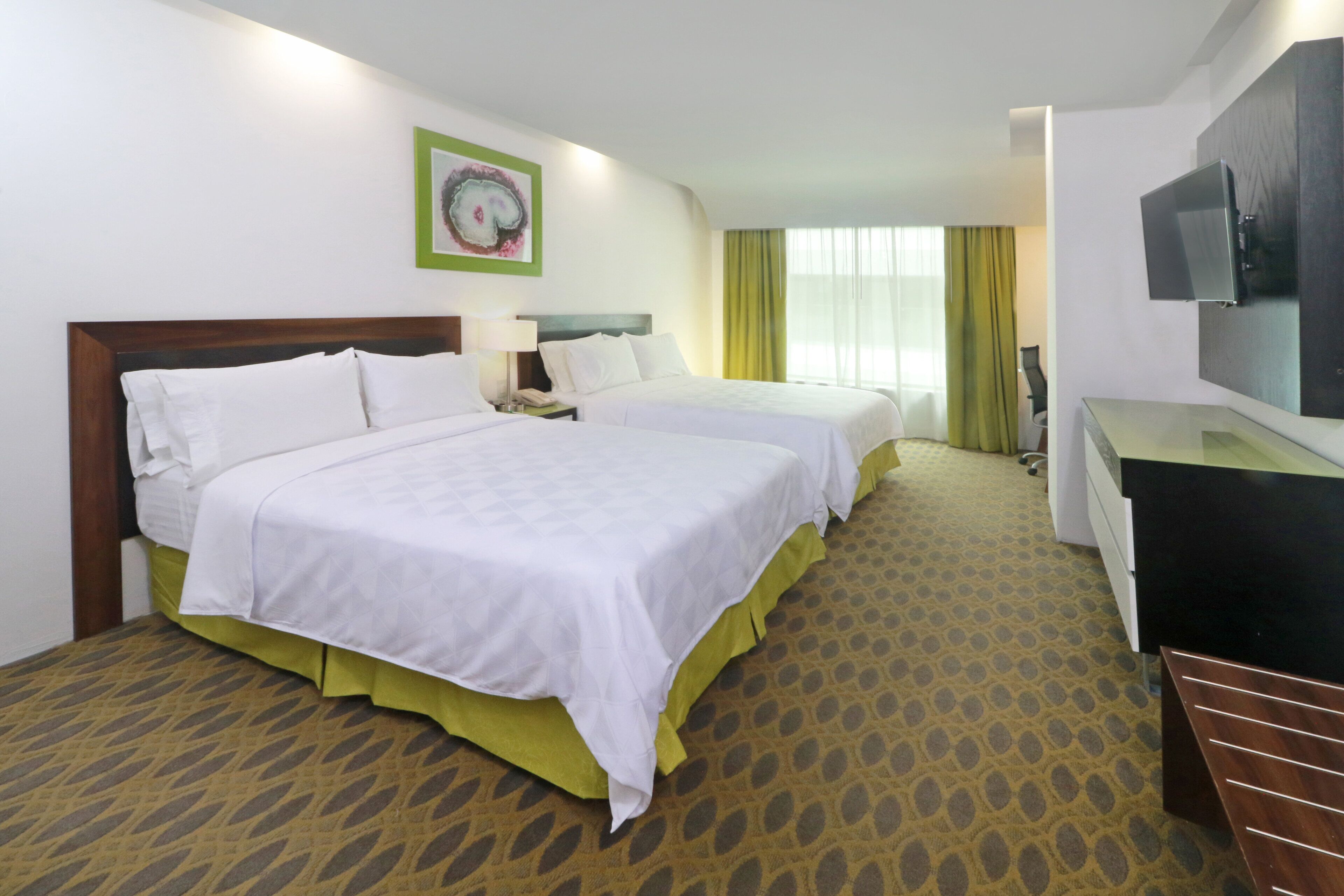 Une chambre d’hôtel avec deux lits, un bureau, une télévision et une moquette à motifs.