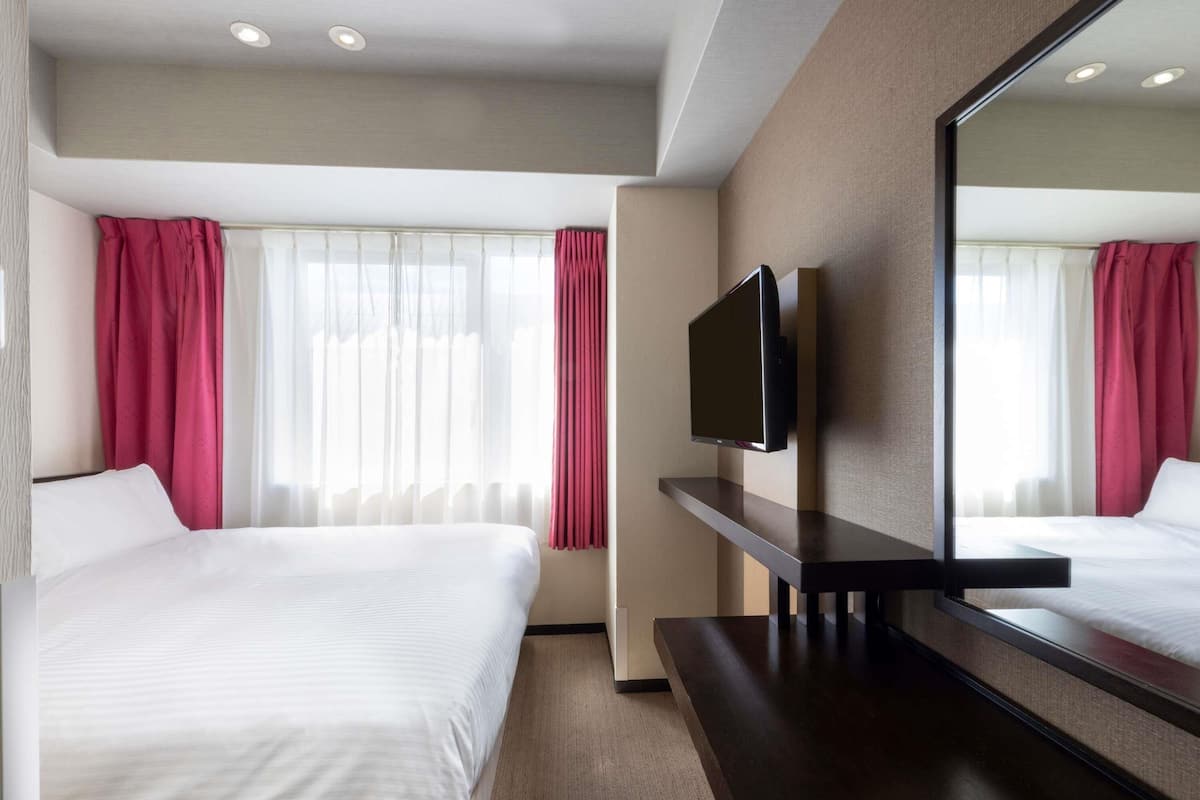 Habitació d'hotel amb dos llits, un televisor de pantalla plana, un mirall gran i una finestra amb cortines.