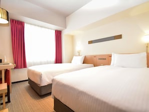 Ein Hotelzimmer mit zwei Betten, einem Schreibtisch, einer Lampe und einem Fenster mit Vorhängen.