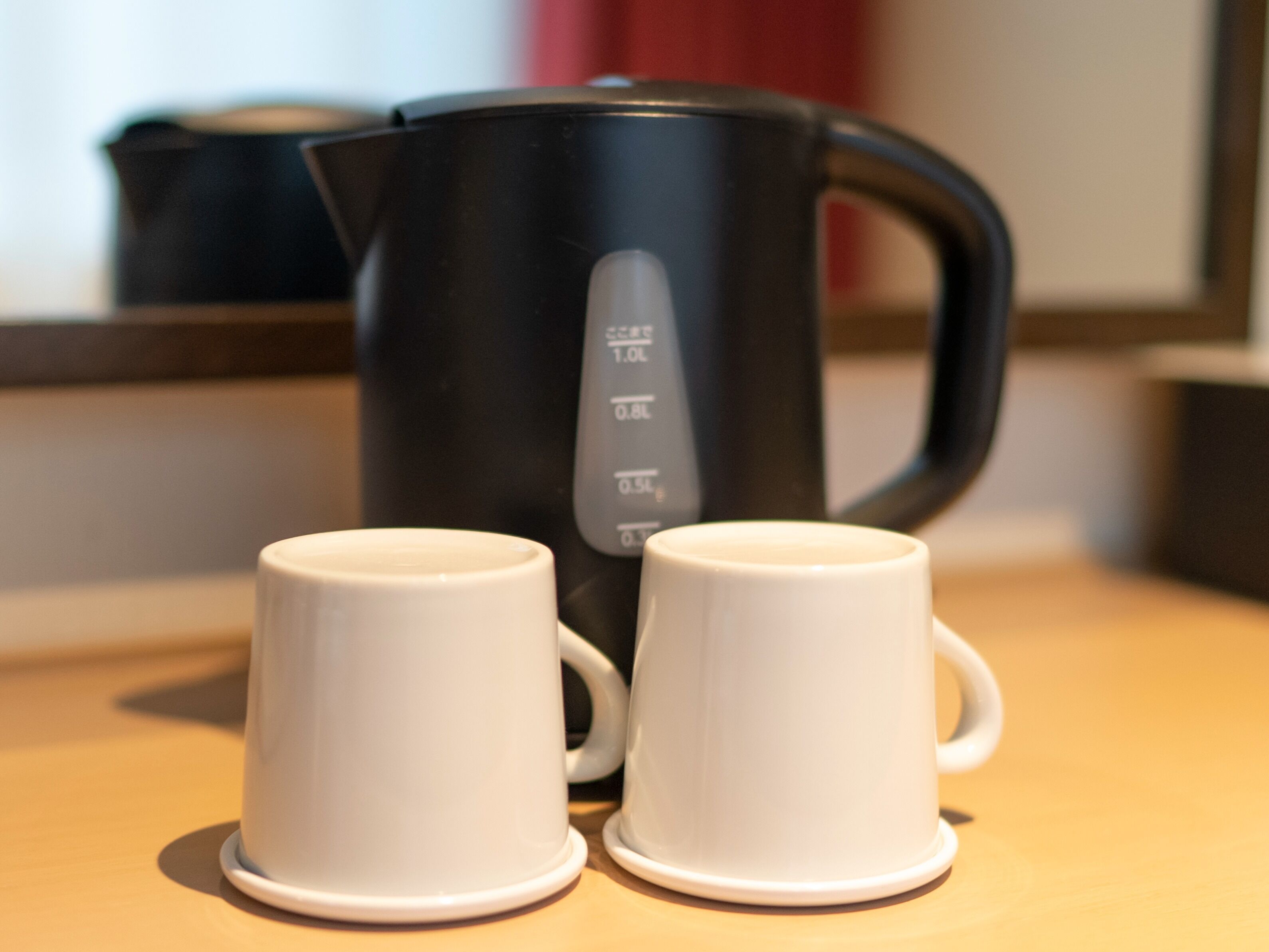 Two white ceramic cups on a wooden surface with a black coffee maker in the background.