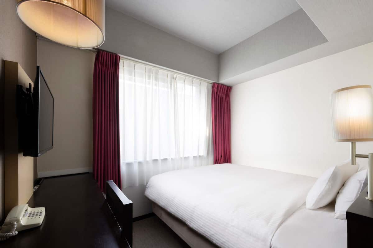 Habitació d'hotel amb un llit, escriptori amb telèfon, televisió i finestra amb cortines.