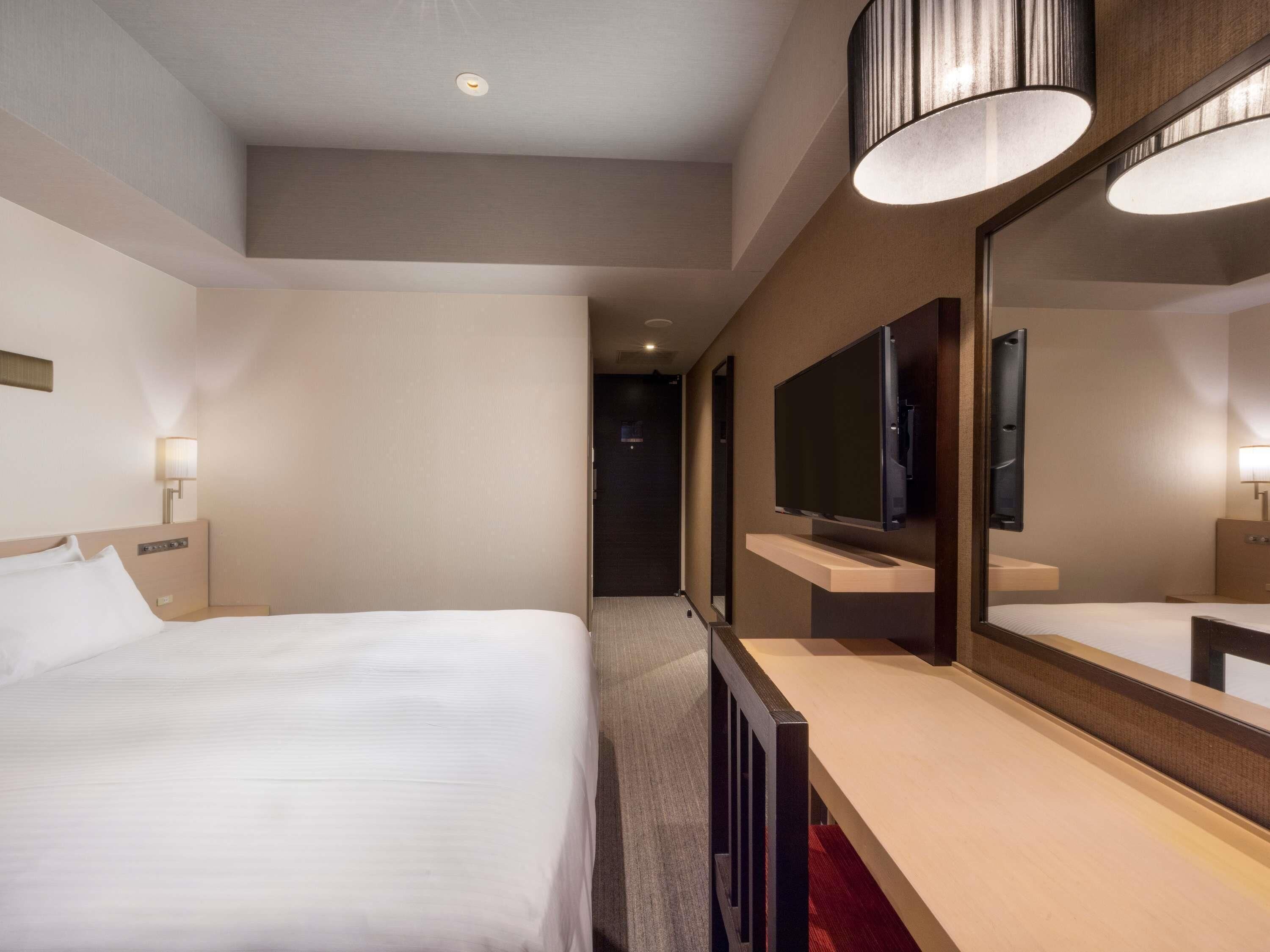 A hotel room with a bed, a large mirror, a TV, and a bathroom counter.