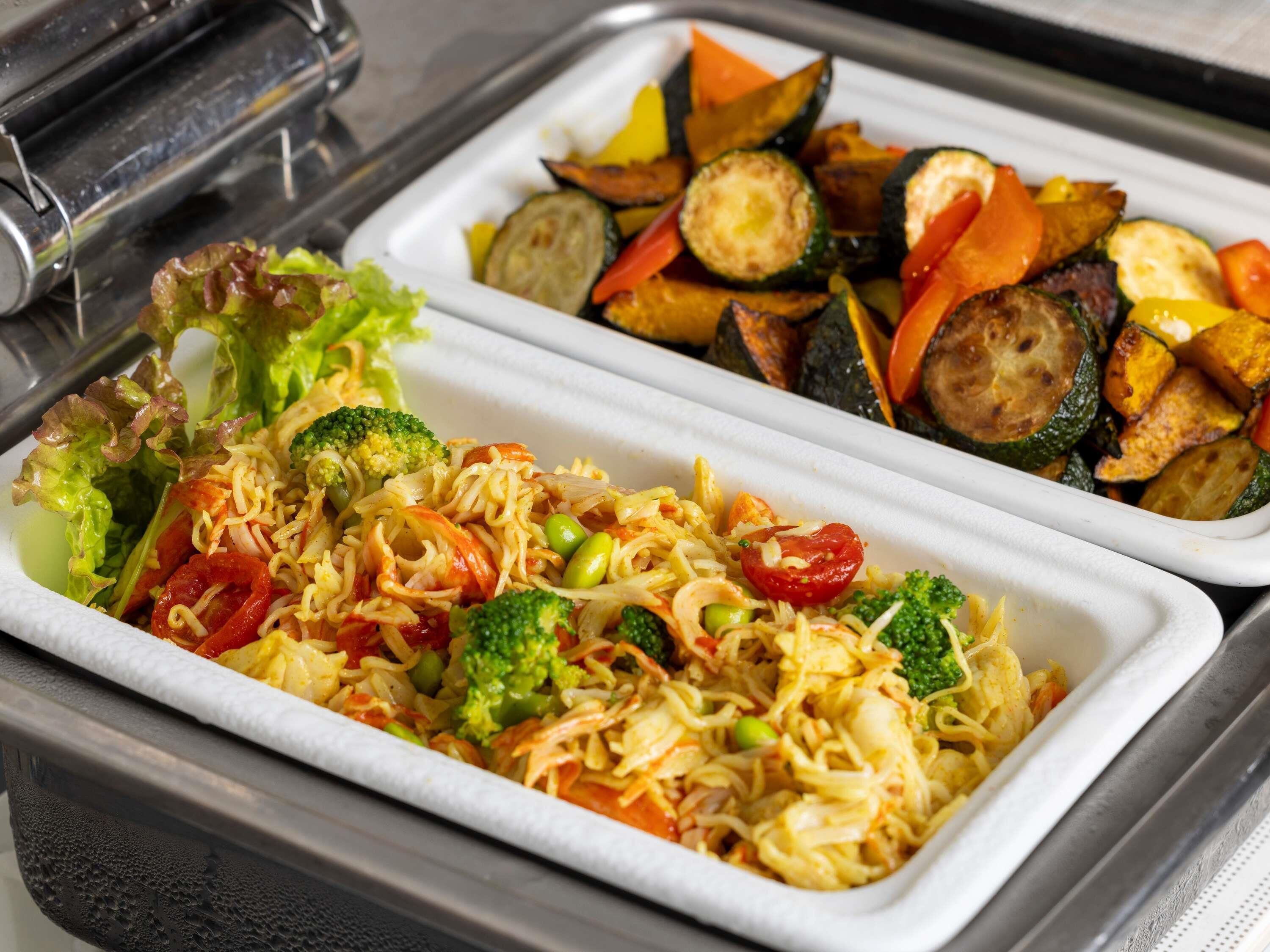 A buffet with noodle dishes, vegetables, and a salad.