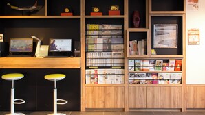 Zona de recepción con estanterías de madera, dos taburetes amarillos y un escritorio con dos monitores.