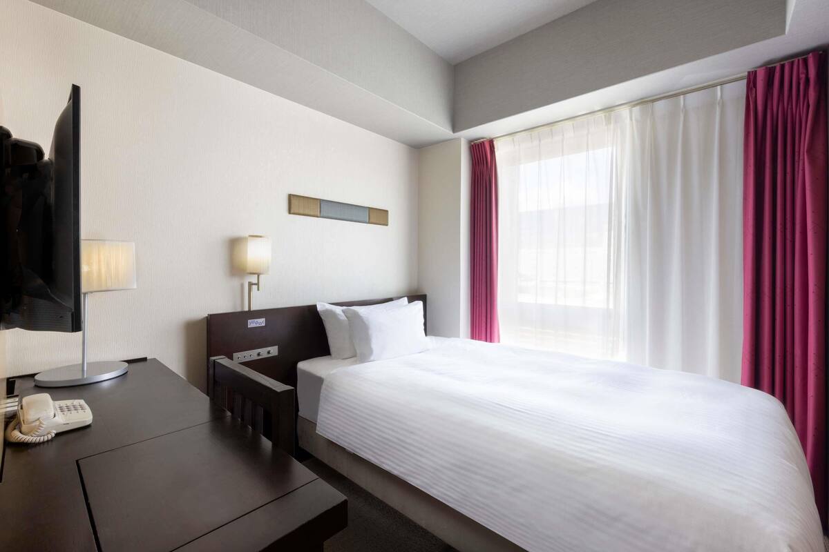 Una habitació d'hotel amb un llit, un escriptori amb un telèfon, una làmpada i una televisió.