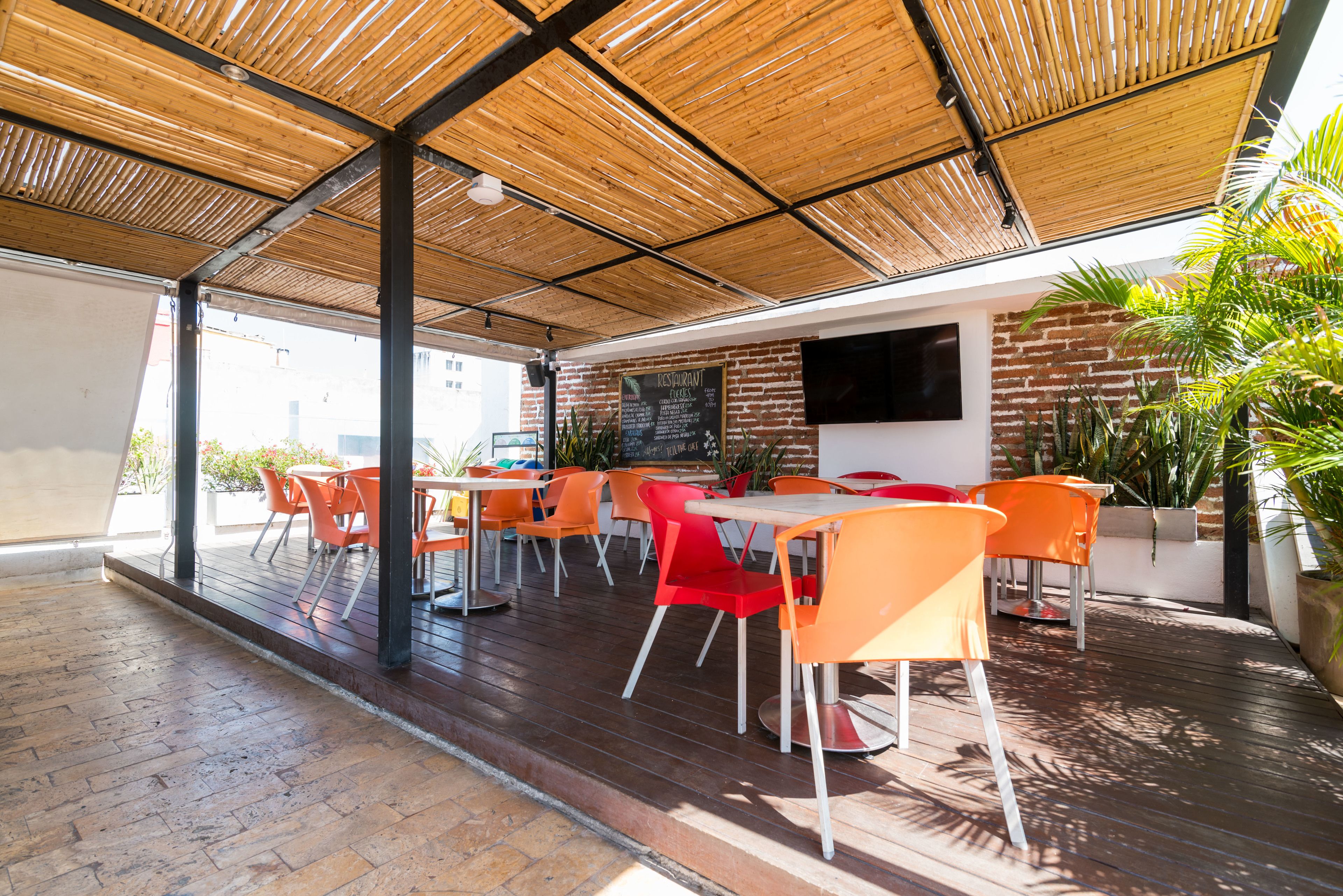 An outdoor dining area with wooden flooring, red and orange chairs, and a brick wall with a mounted TV.