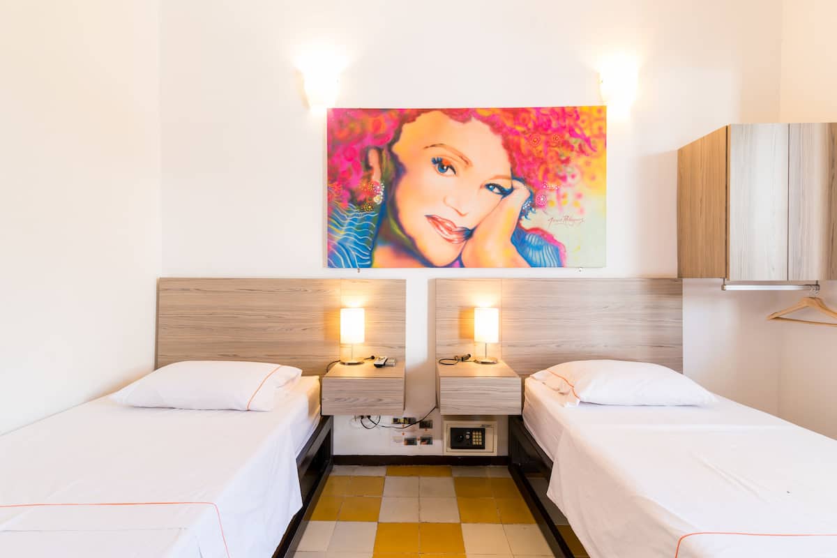 A hotel room with two beds, a painting on the wall, and a wooden headboard.