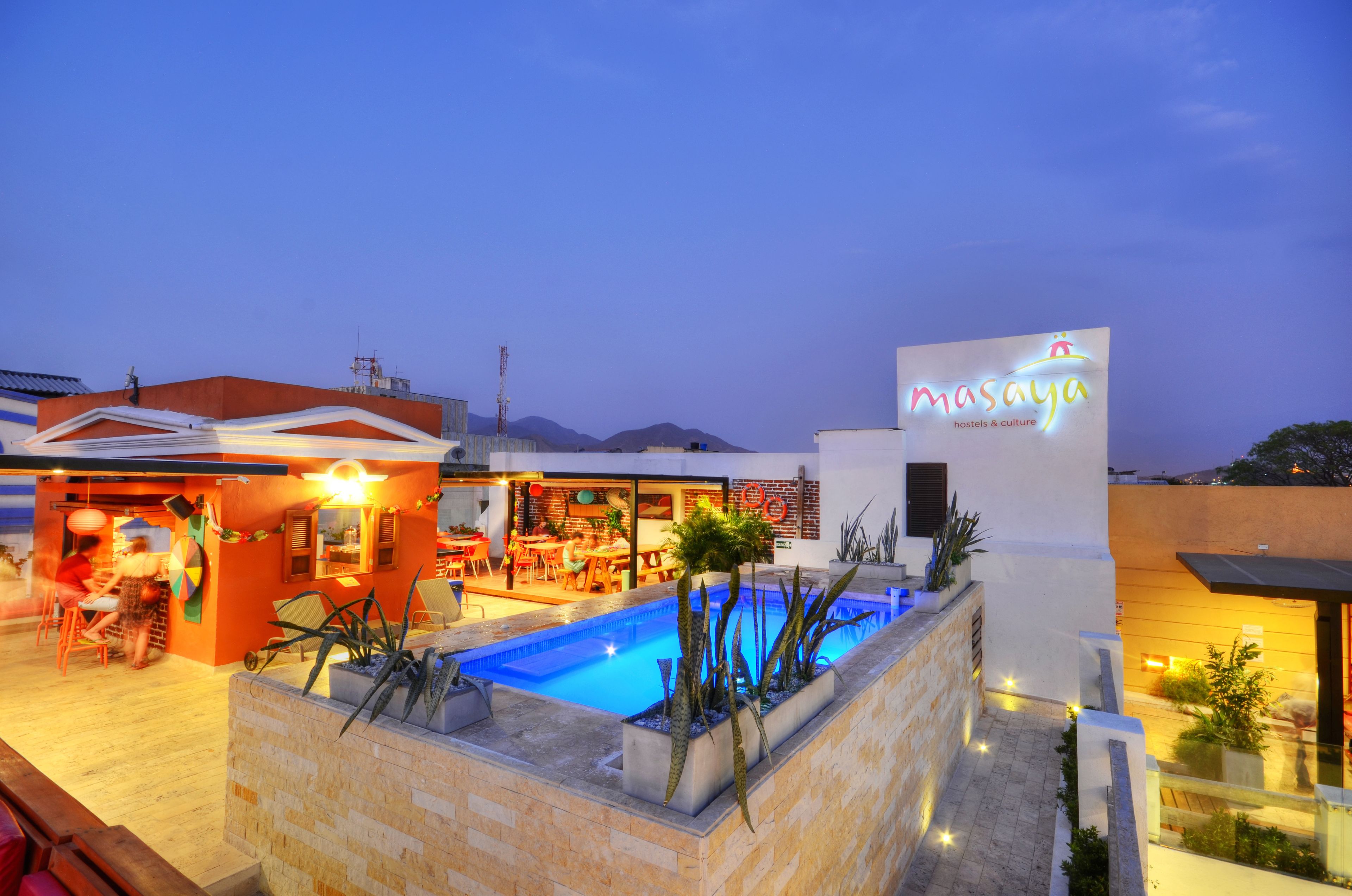 A hotel with a swimming pool, outdoor seating, and a sign that reads "Masaya hostels & culture".