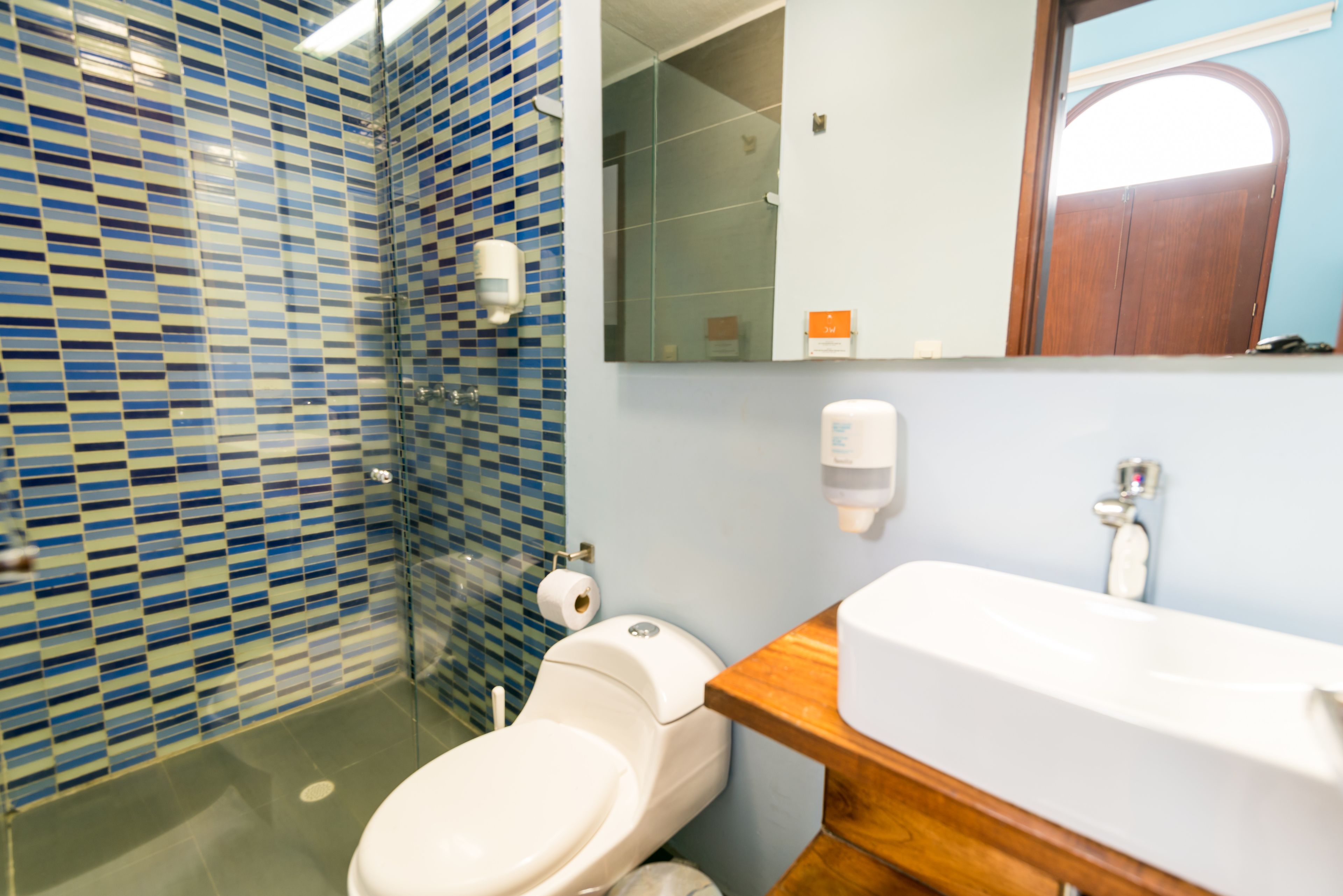 Un baño con pared de azulejos, inodoro, lavabo y espejo.