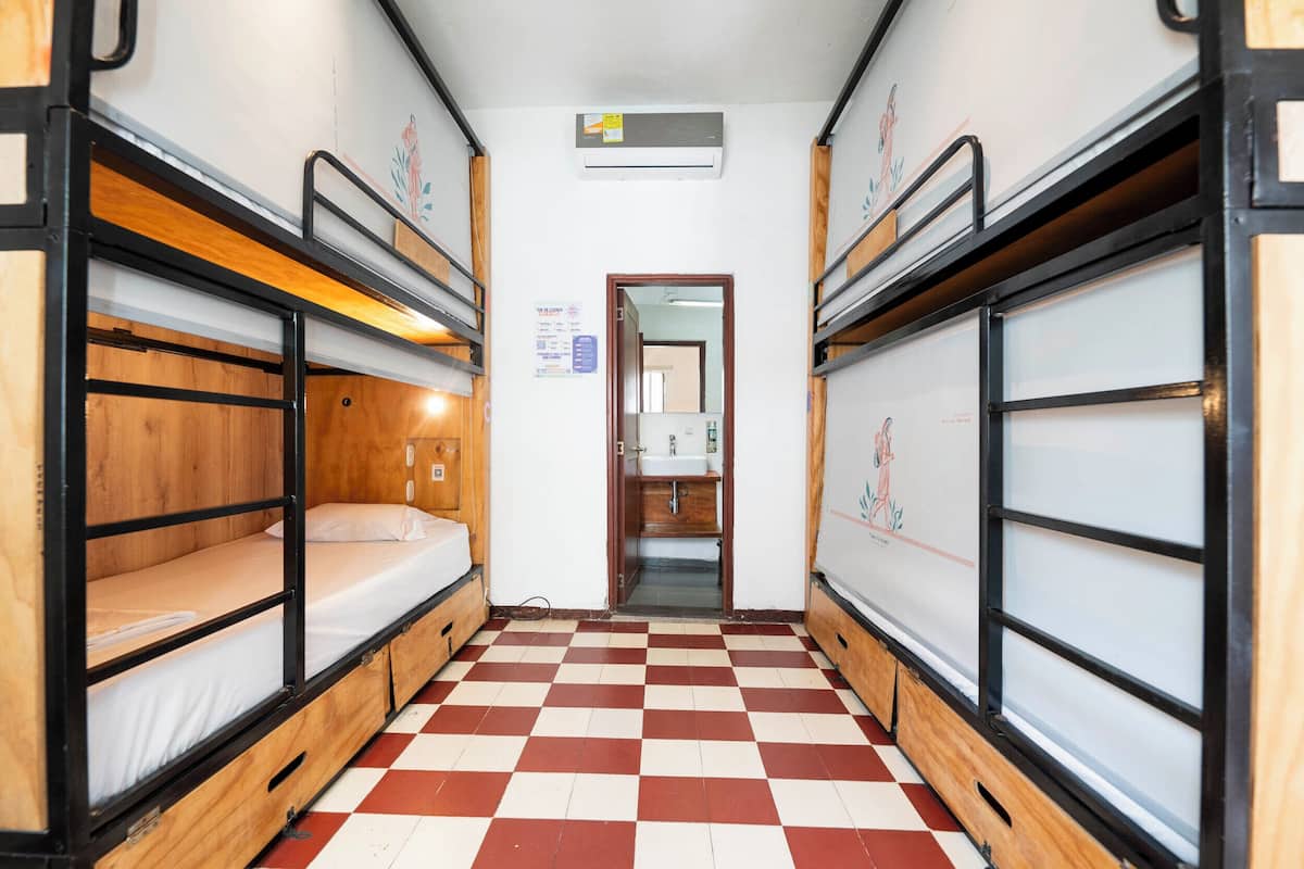 A narrow corridor with bunk beds on either side, a checkered floor, and a door leading to a bathroom.