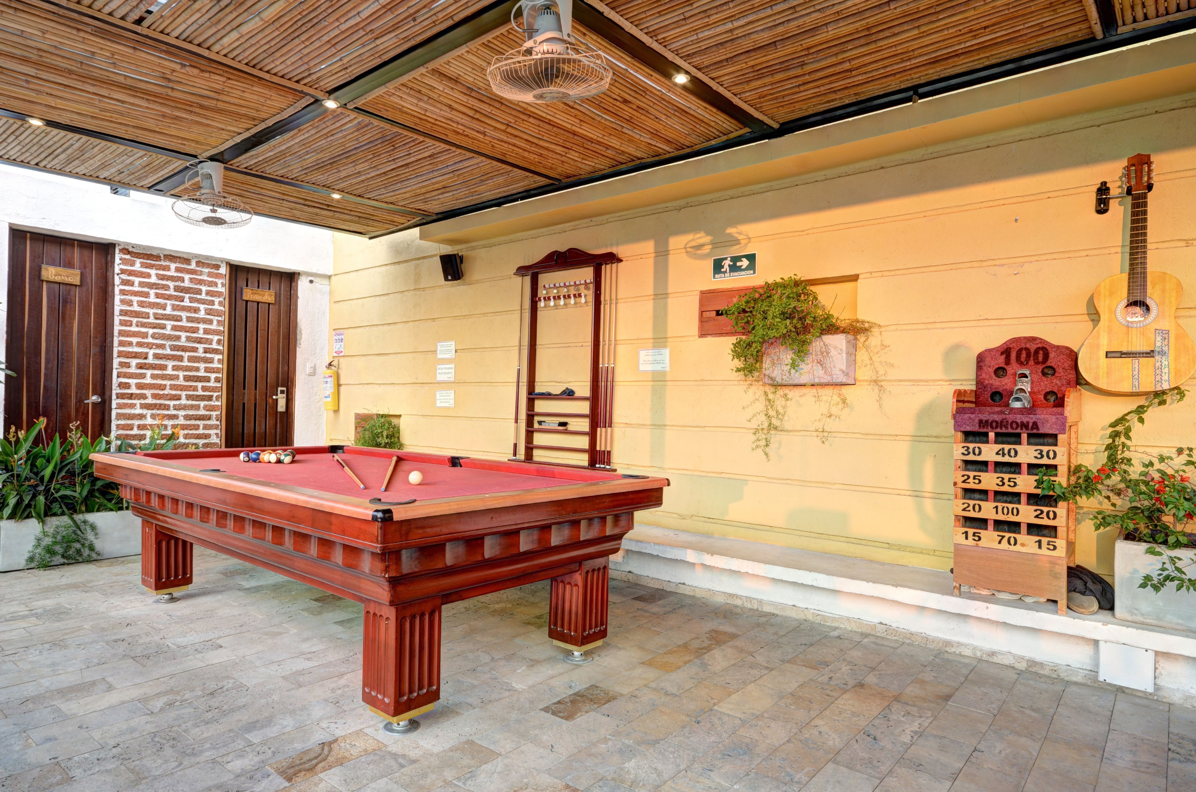 A pool table in an outdoor area with a brick wall, wooden doors, and a guitar hanging on the wall.