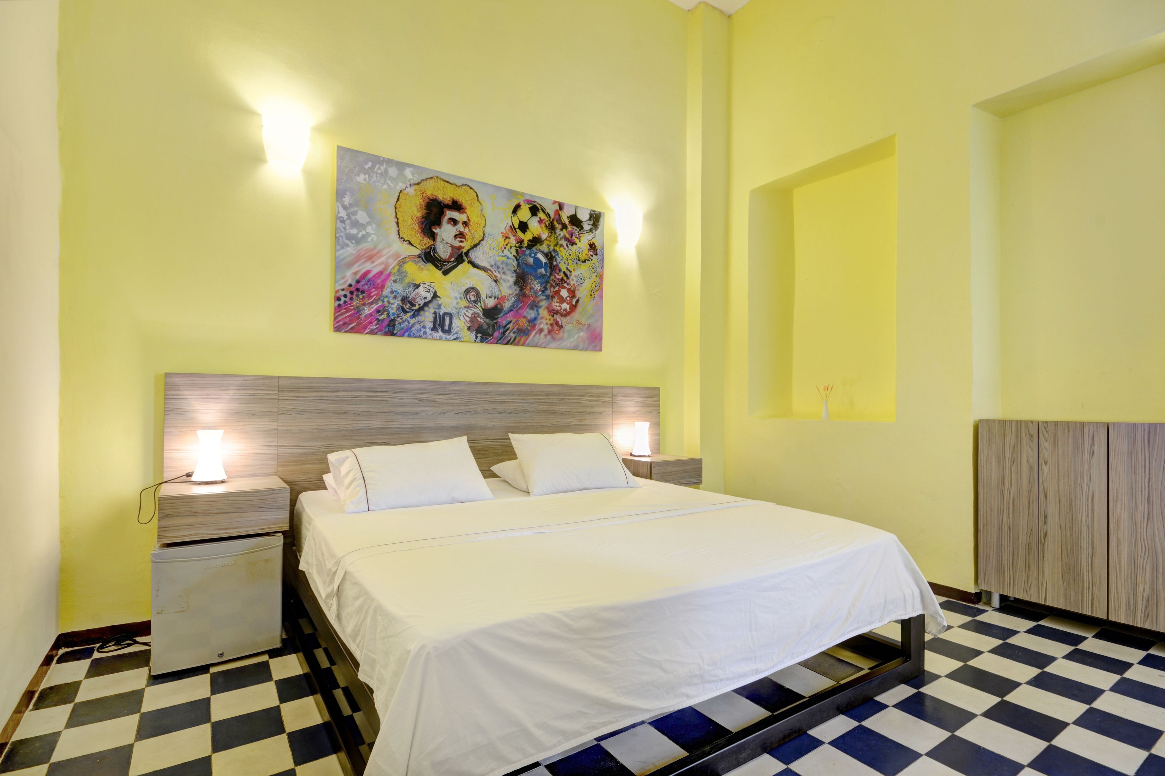 A hotel room with a bed, a nightstand, a wall-mounted painting, and a checkered floor.