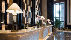 Un comptoir d’accueil en marbre agrémenté de lampes, d’une plante en pot et offrant une vue sur le hall d’entrée.