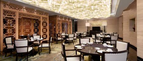 Una amplia sala de conferencias con mesas y sillas redondas, paneles de madera decorativos e iluminación ornamental en el techo.