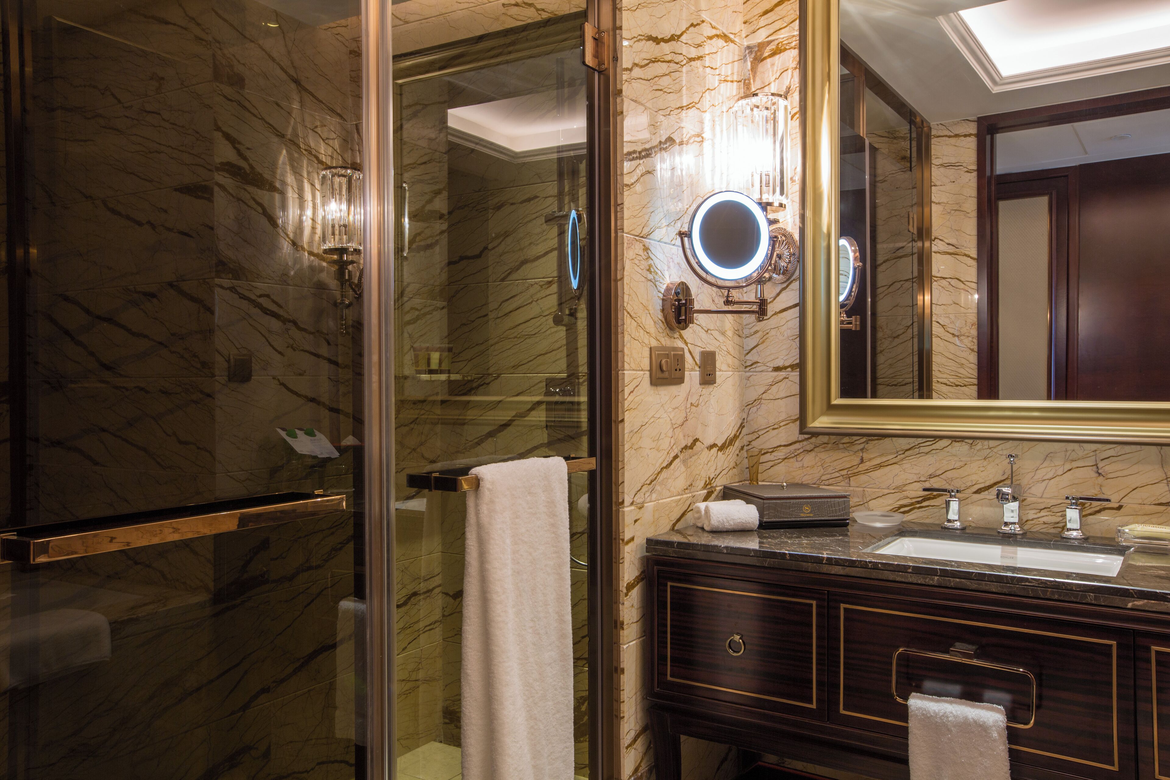 A bathroom with a glass-enclosed shower, marble walls, a large mirror, and a dark wooden vanity with a sink.