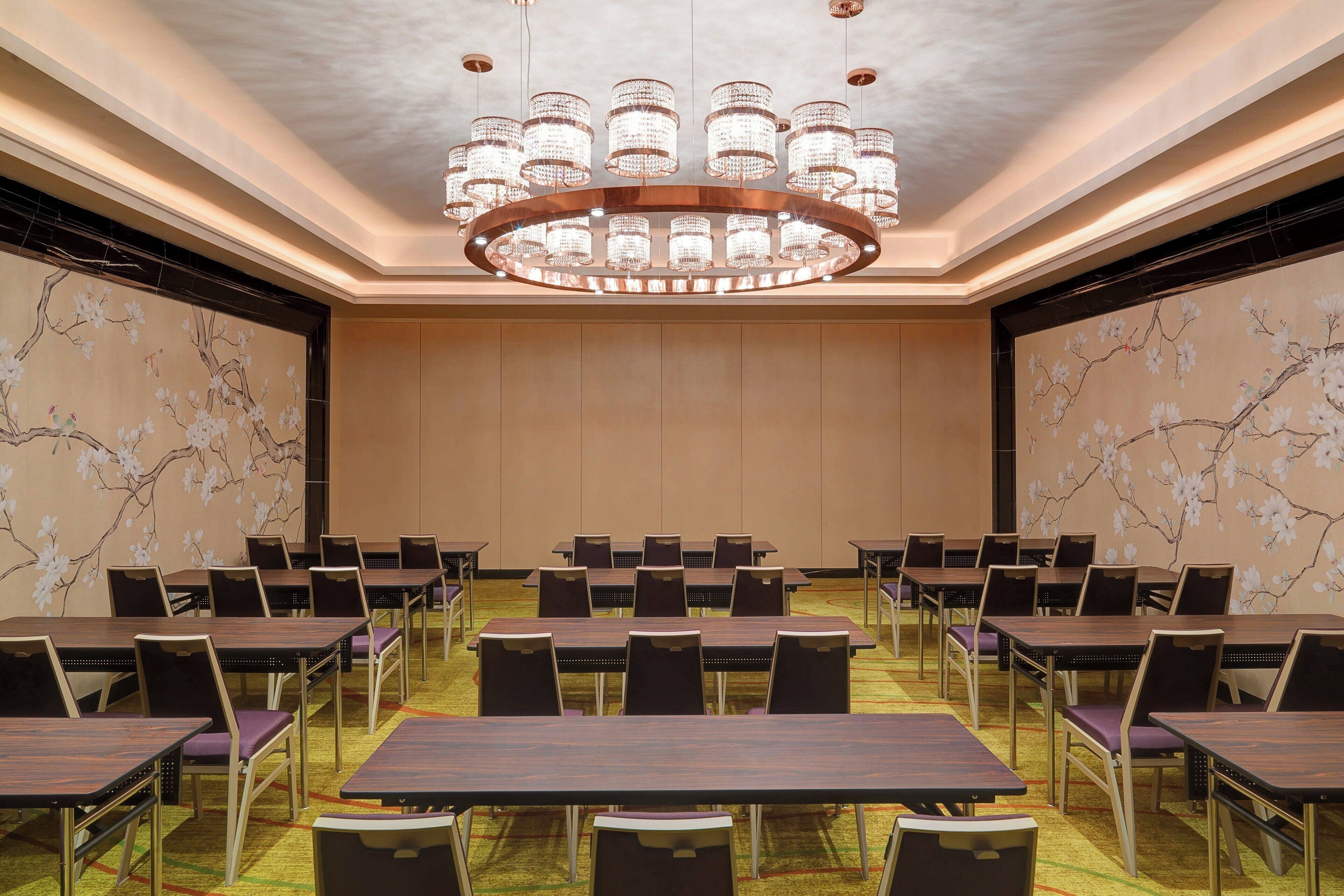 Een congreszaal met meerdere tafels en stoelen, een grote kroonluchter en bloemistische wanddecoratie.