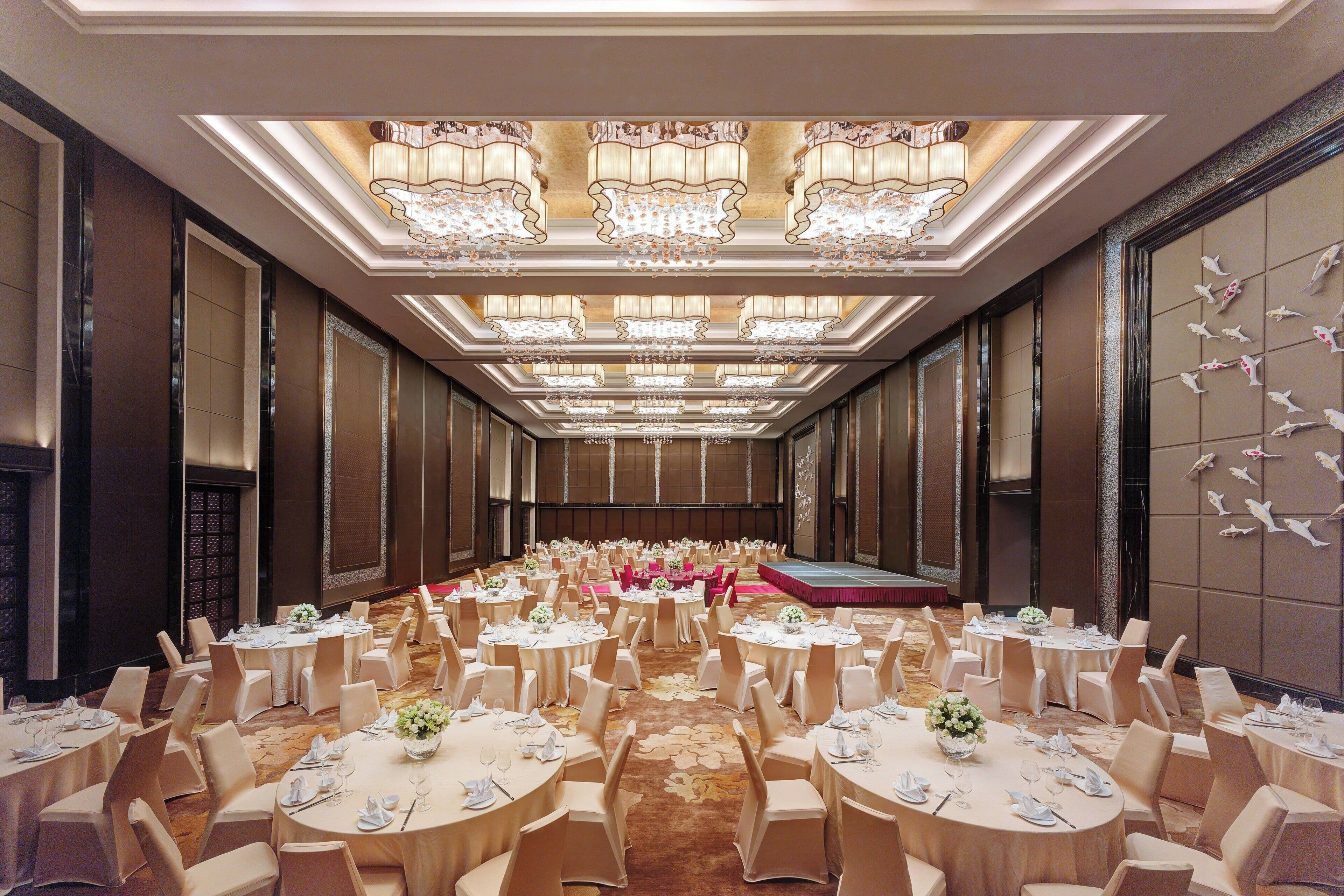 Un salón de banquetes con mesas redondas, sillas y un escenario.