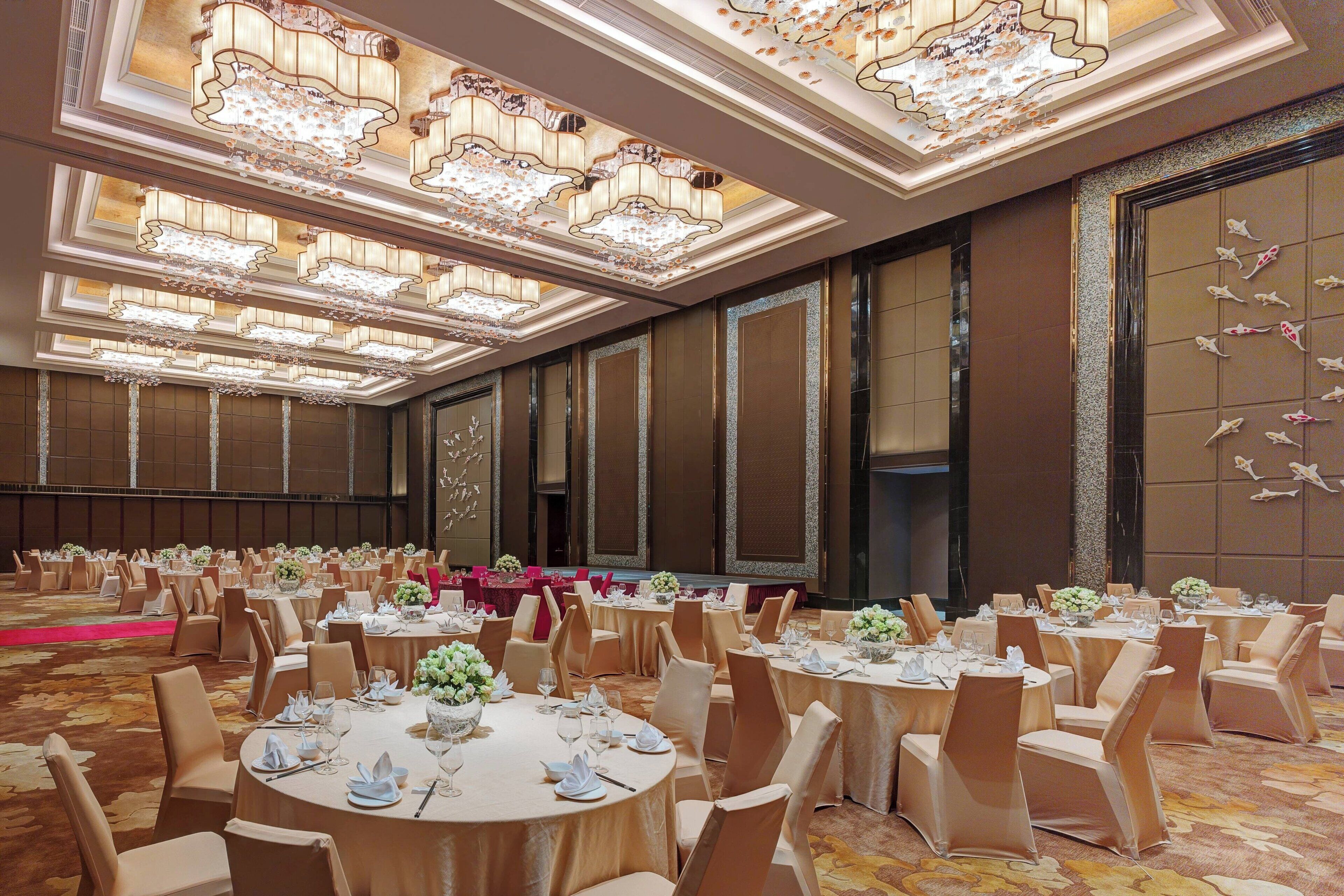 Un salón de banquetes con mesas redondas, sillas color beige y candelabros.