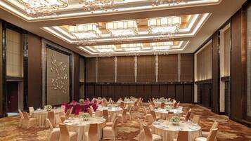 Une salle de banquet avec des tables rondes, des chaises de couleur beige et des lustres.