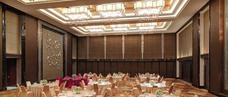A banquet hall with round tables, beige chairs, and chandeliers.