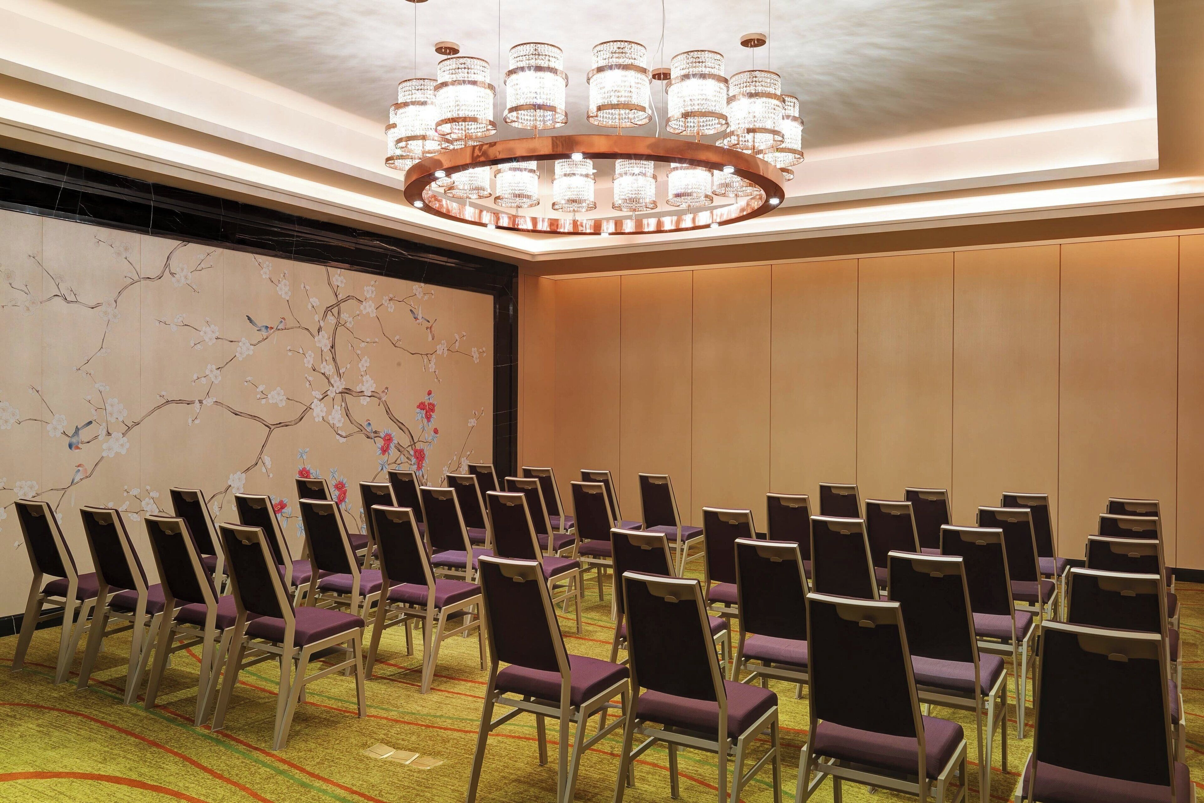 Ein Konferenzraum mit Reihen lila Stühle, einer großen Leinwand und einer Kristallleuchter.